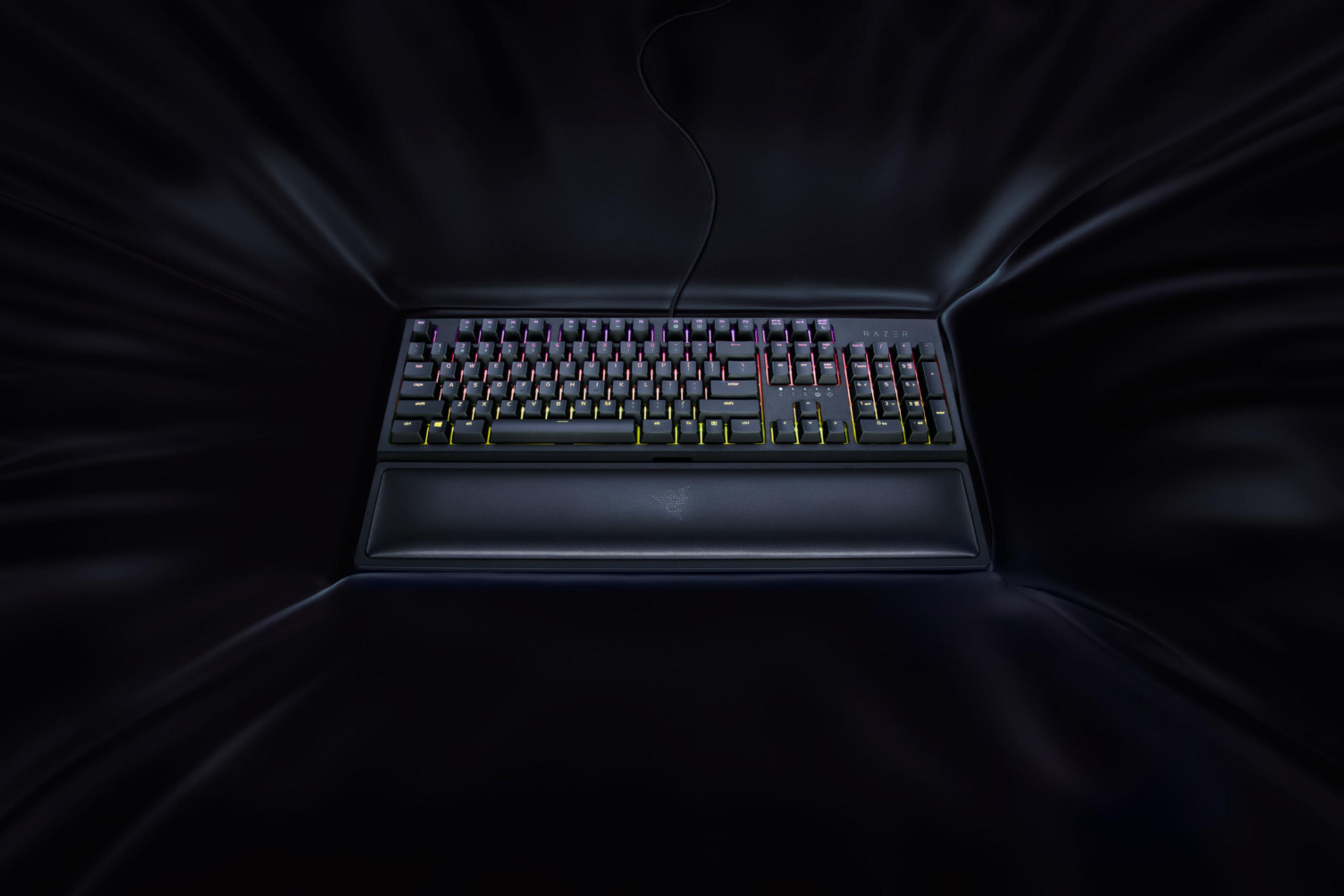 Eine schwarze Tastatur mit RGB-Beleuchtung und Handgelenkauflage auf dunklem Stoff.