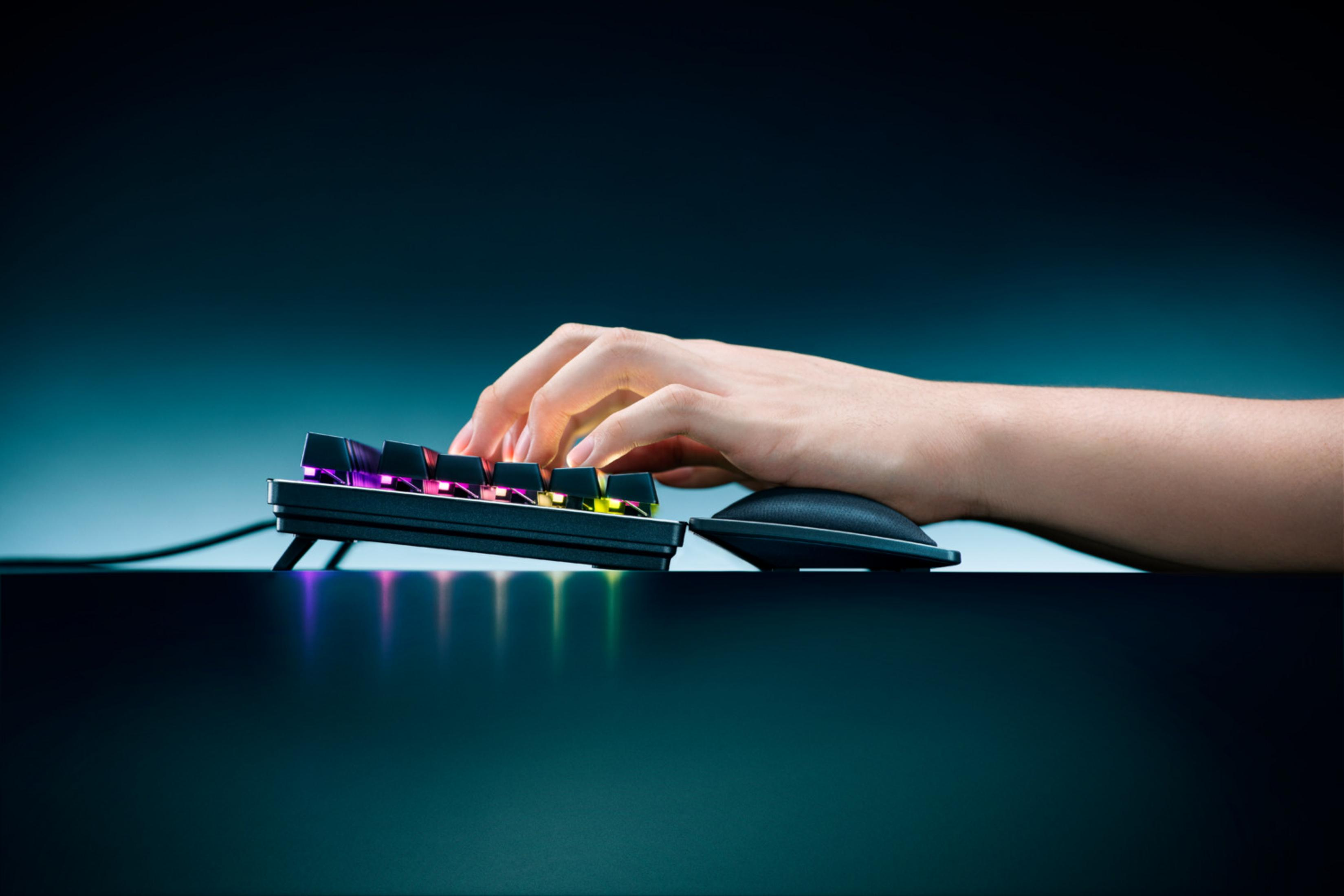 Une main tape sur un clavier rétroéclairé, avec un repose-poignet à côté.