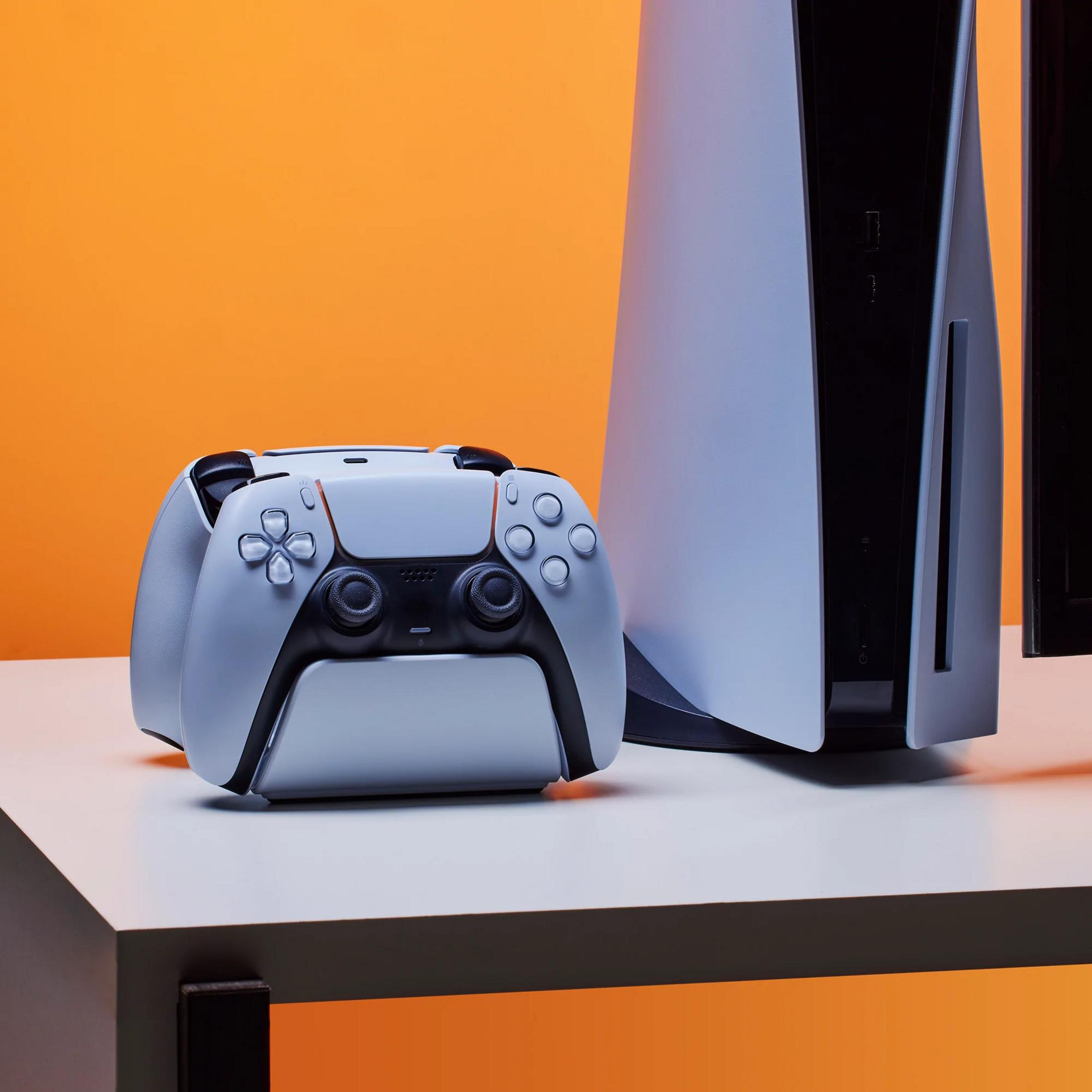 Eine weiße Spielkonsole und ein Controller stehen auf einem Tisch vor orangefarbenem Hintergrund.