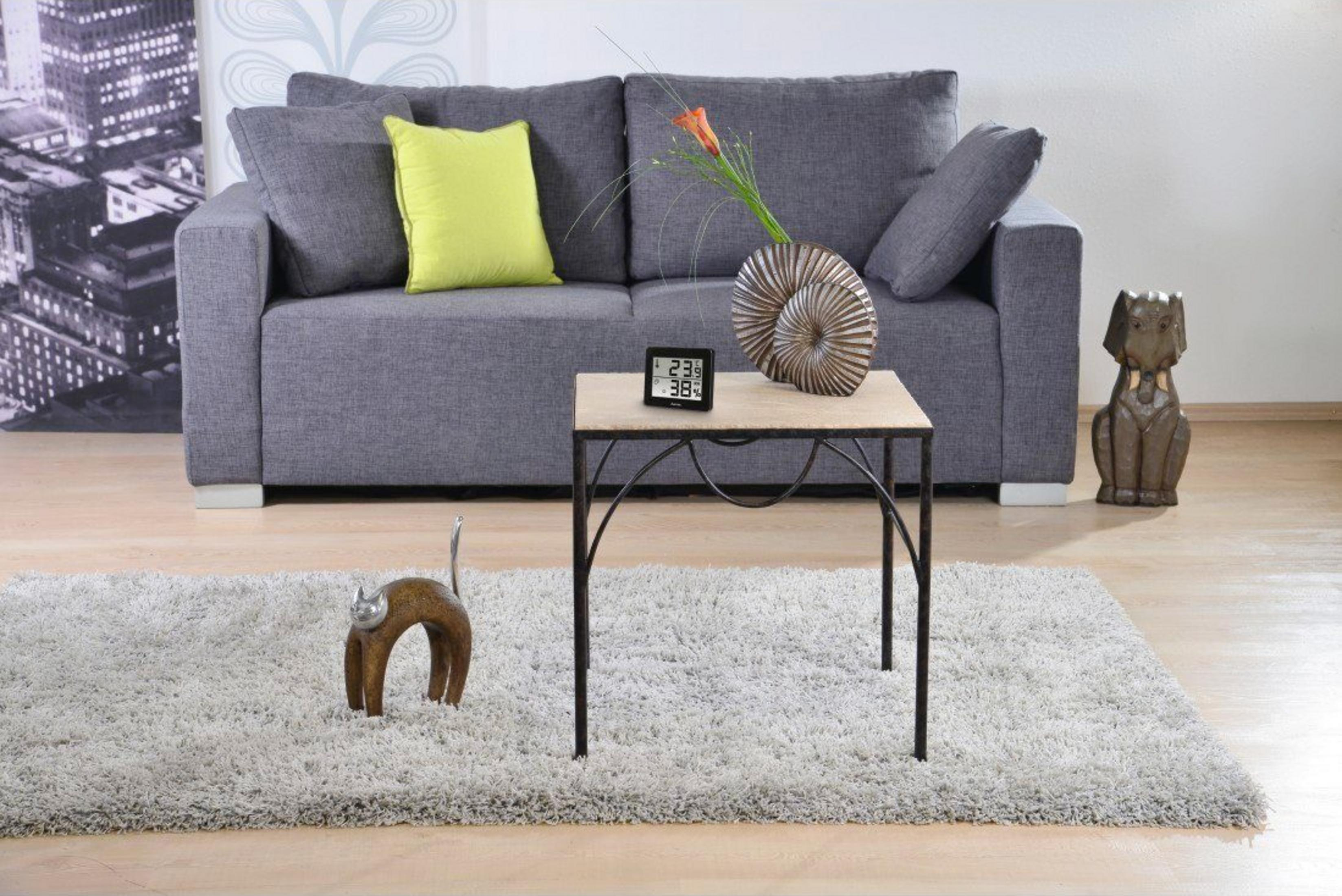 Szara sofa z poduszkami, stolik boczny z wazonem, zegarem i ozdobą kota.