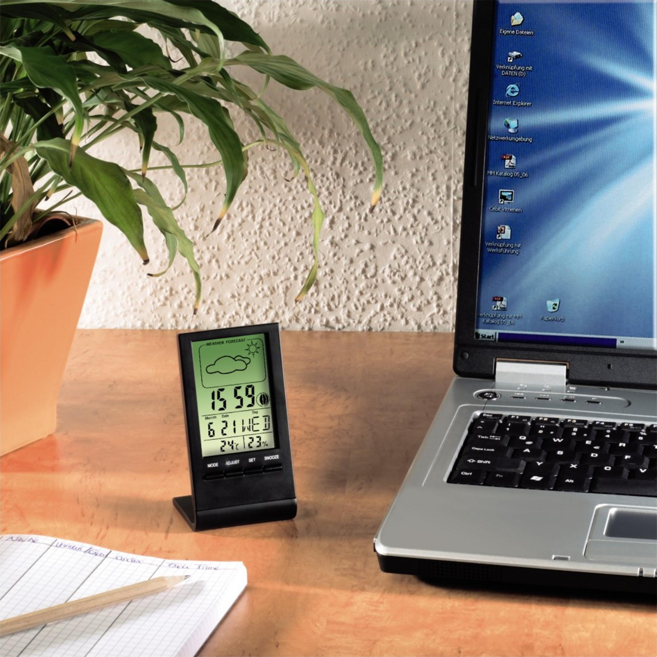 Laptop, stacja pogodowa i roślina na biurku.