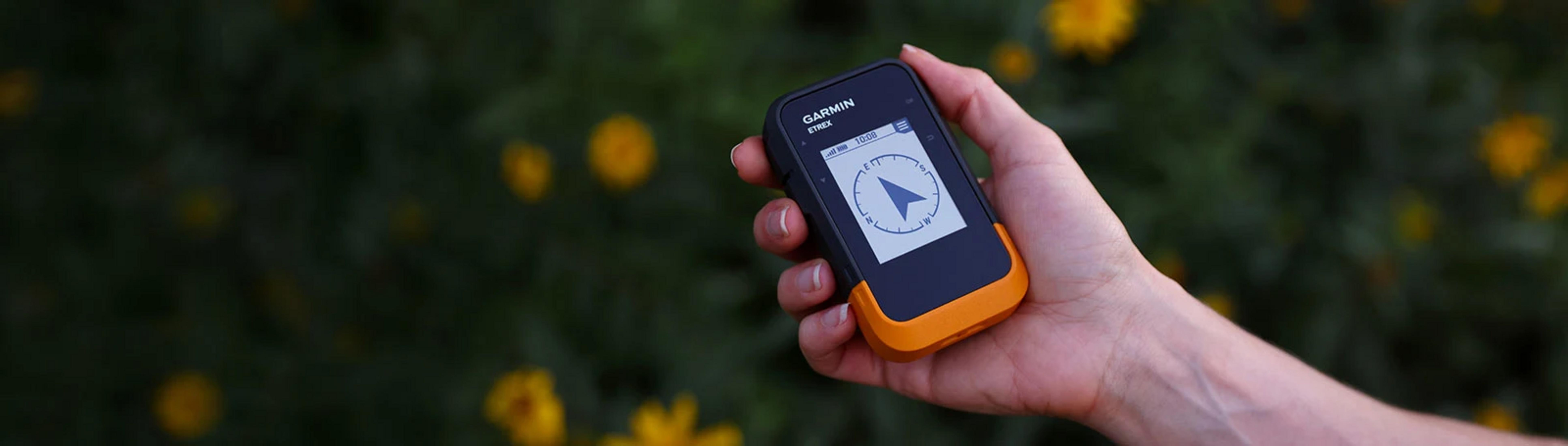 Hand hält Garmin Etrex GPS-Gerät mit Kompassanzeige vor dunklem Hintergrund.