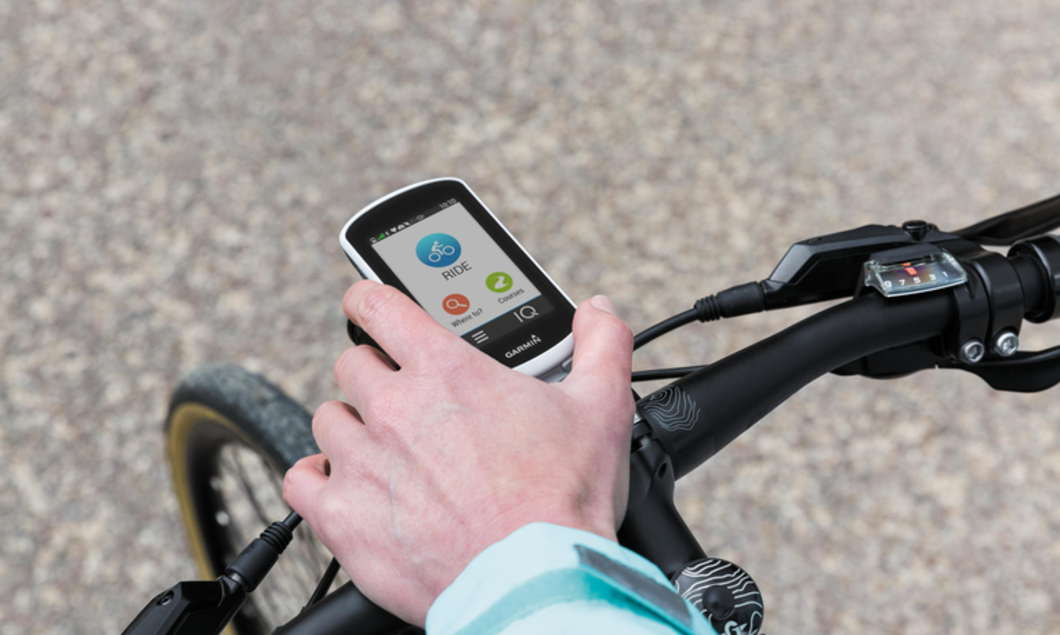 Person bedient Fahrradcomputer am Lenker vor Schotterhintergrund.
