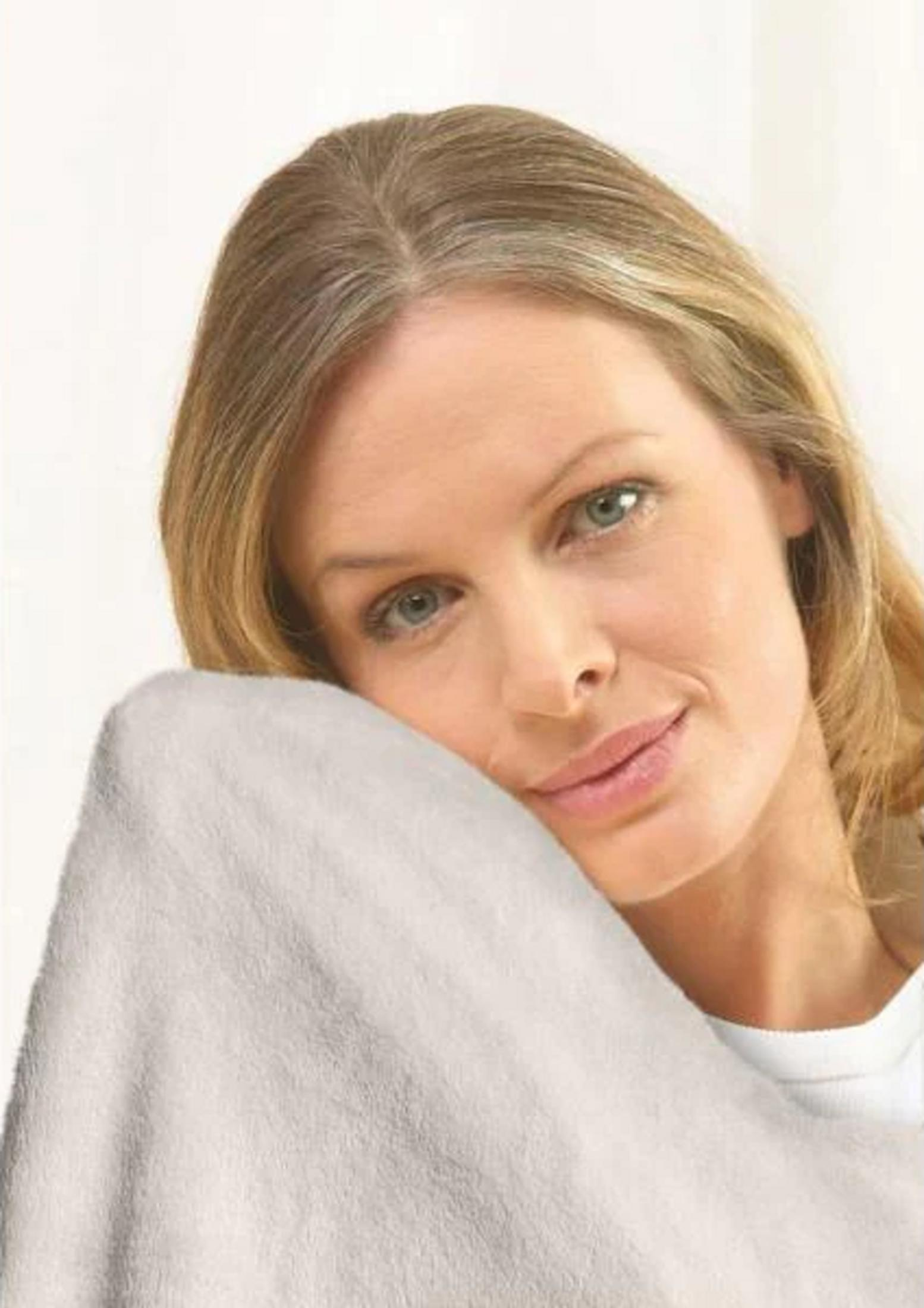 Una donna bionda appoggia il mento su una coperta grigio chiaro.