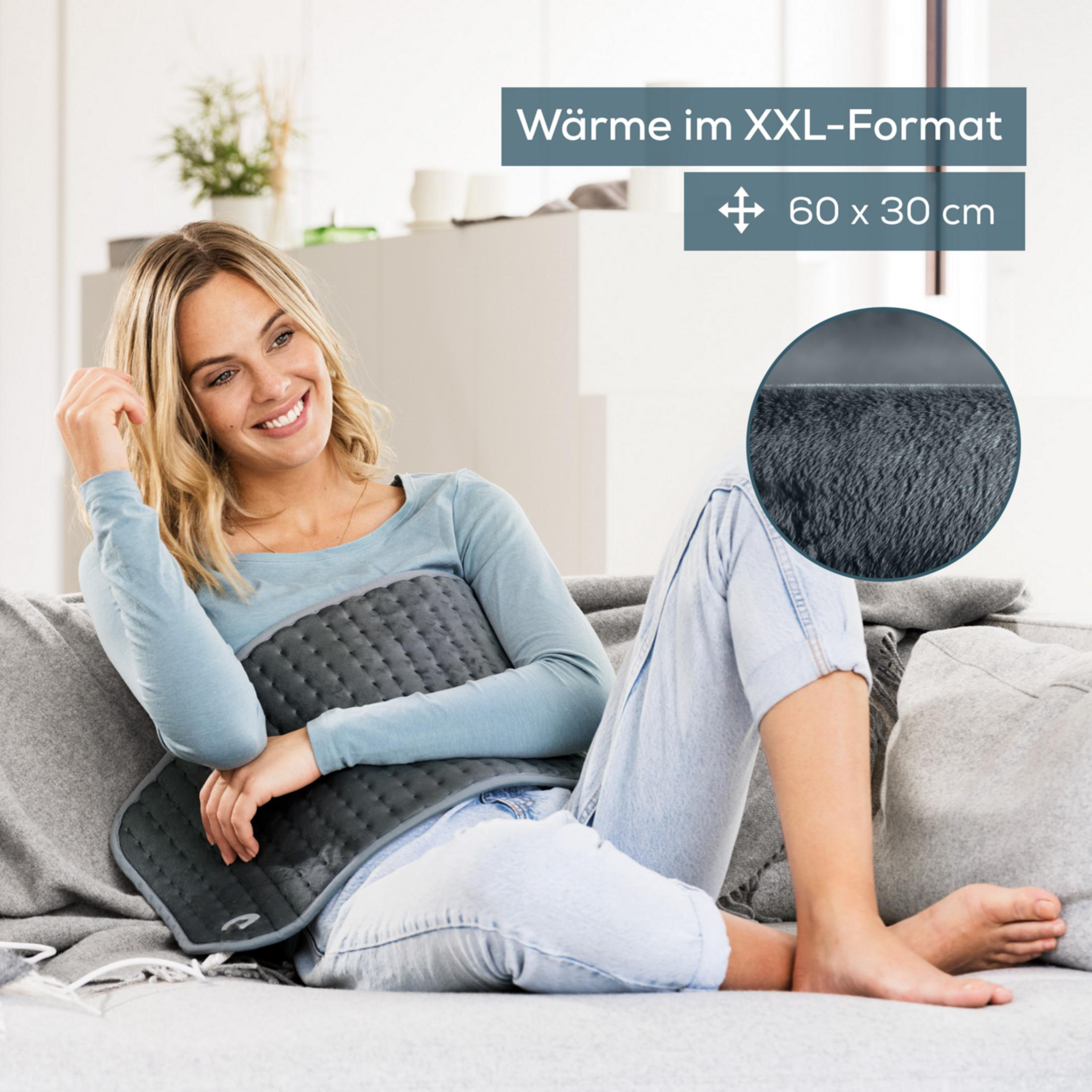 Donna su divano con termoforo. "Calore formato XXL".