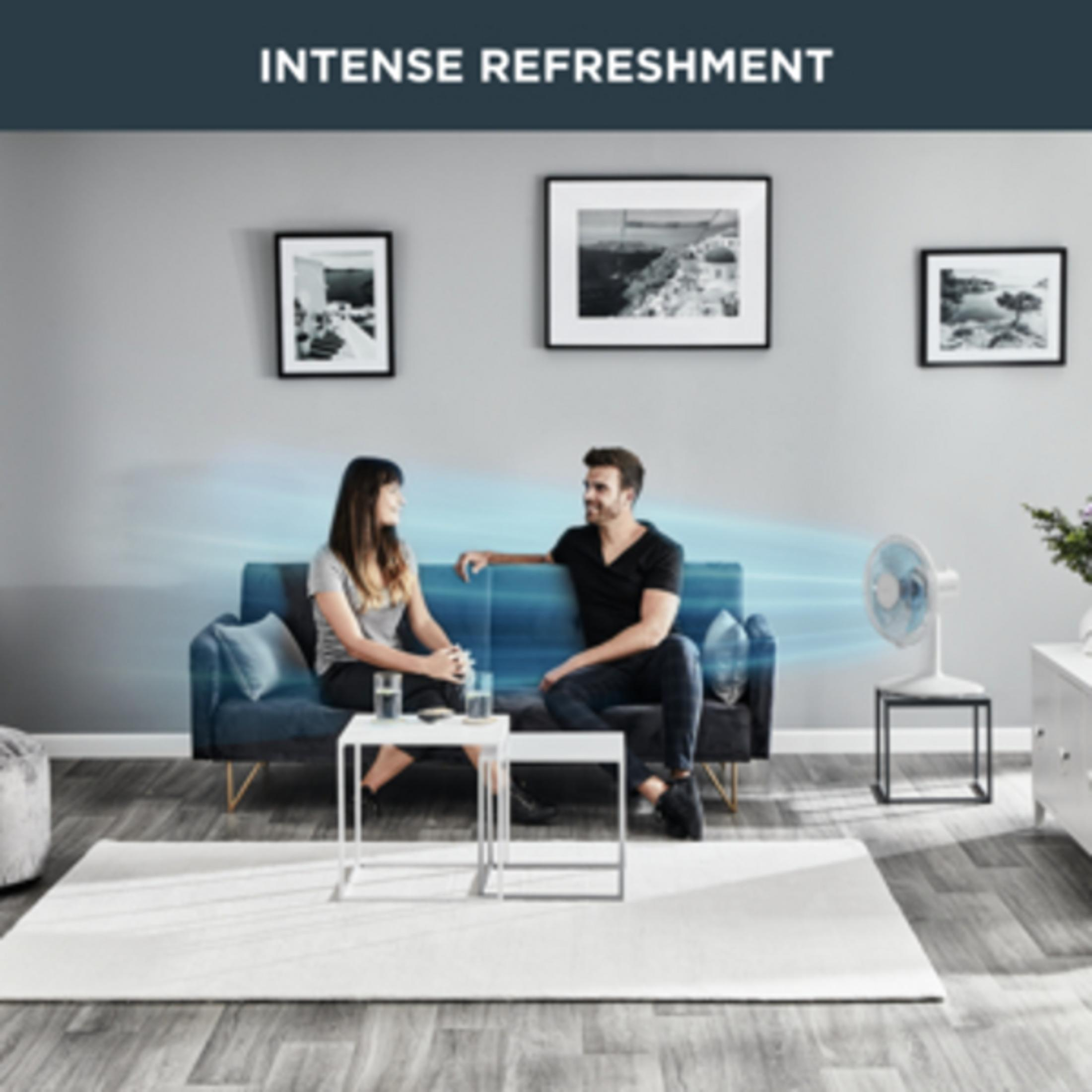 Mężczyzna i kobieta siedzą na sofie, wentylator dmucha powietrzem.