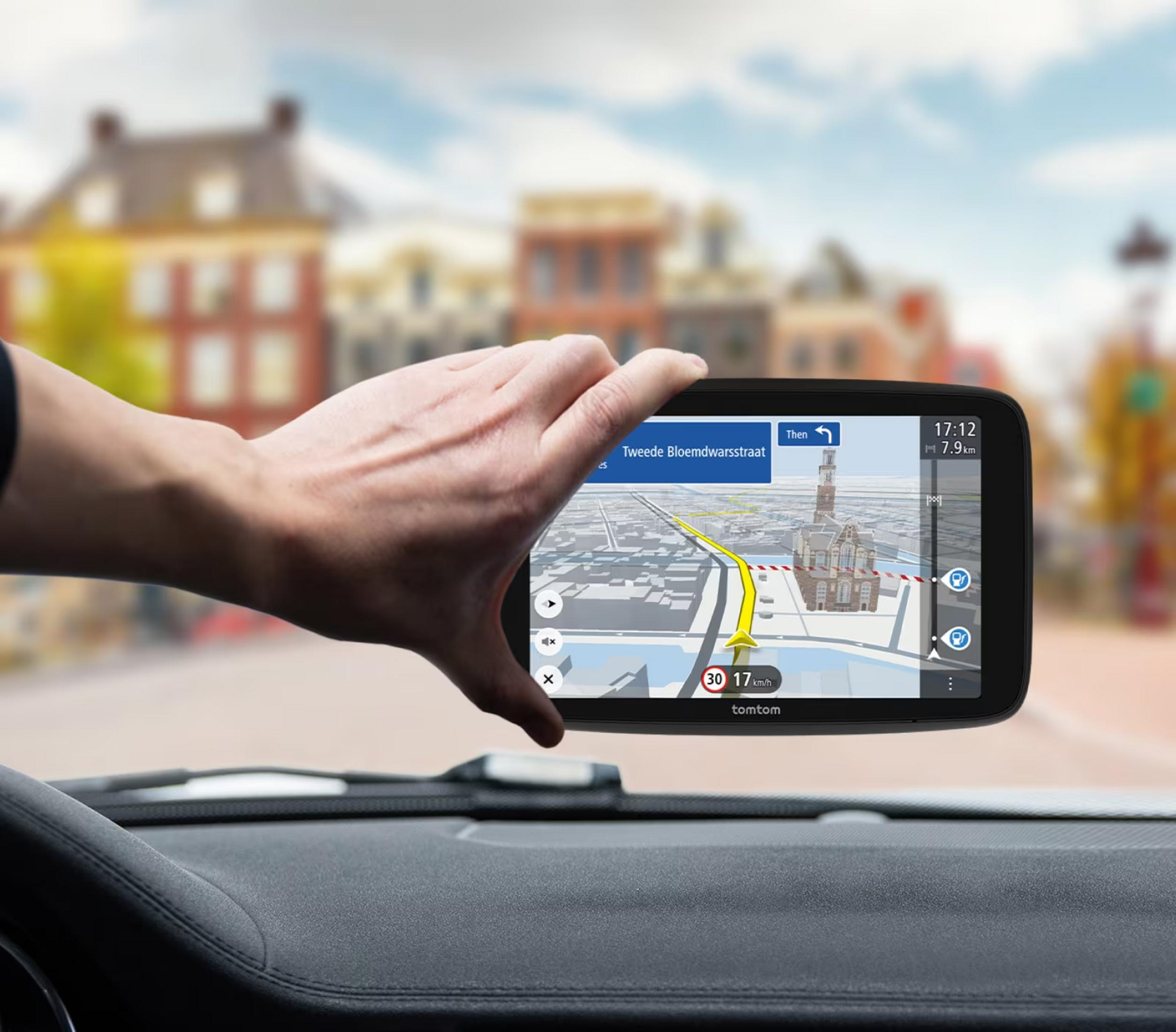 A person holds a TomTom GPS device showing a city map and route.