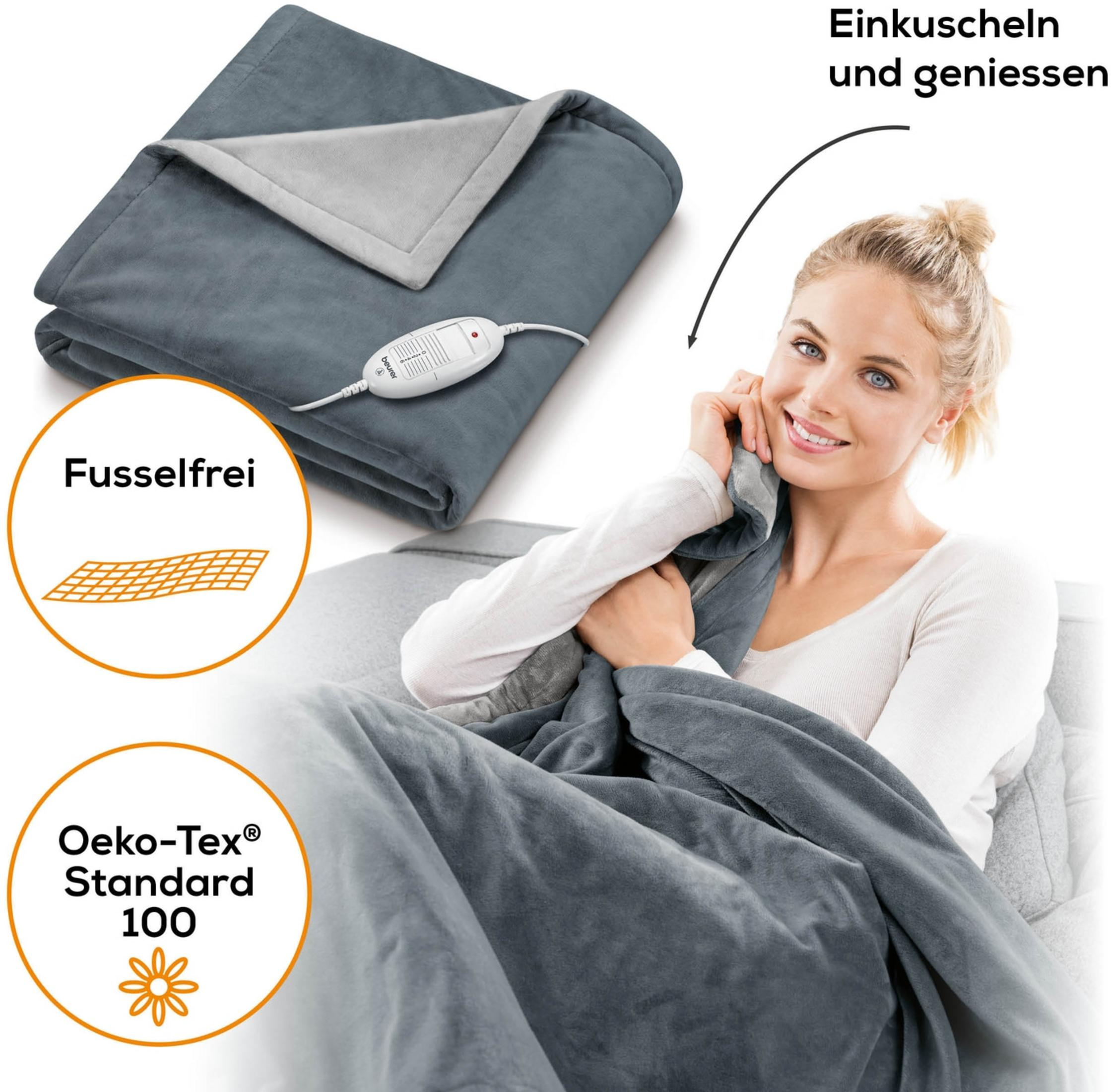 A woman cuddles in a grey electric blanket with a remote control.