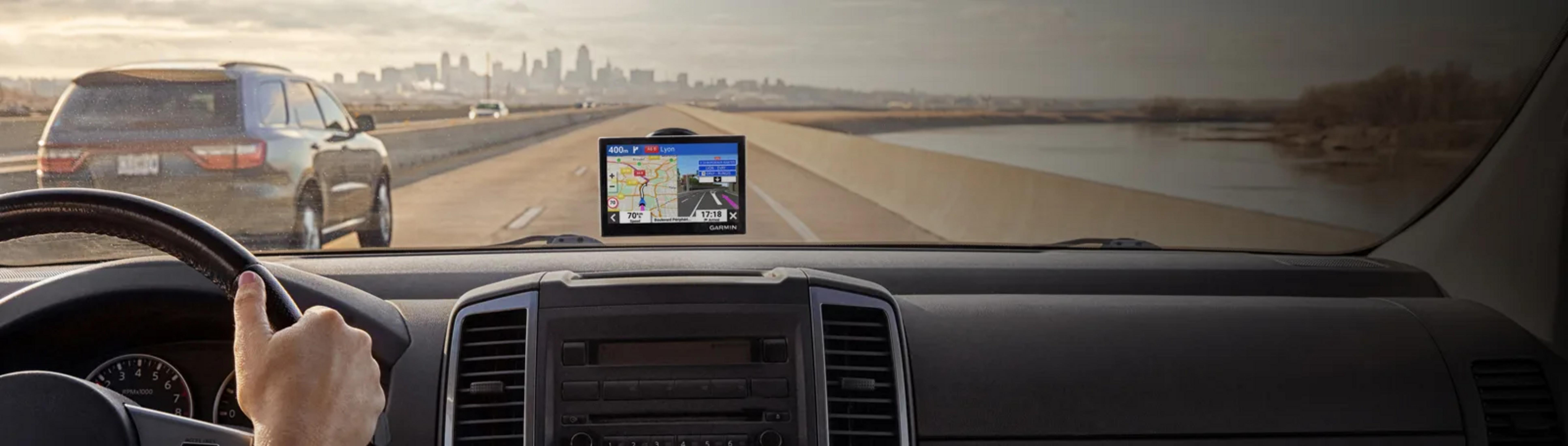 Mano del conducente sul volante, GPS mostra mappa, autostrada, città in lontananza.