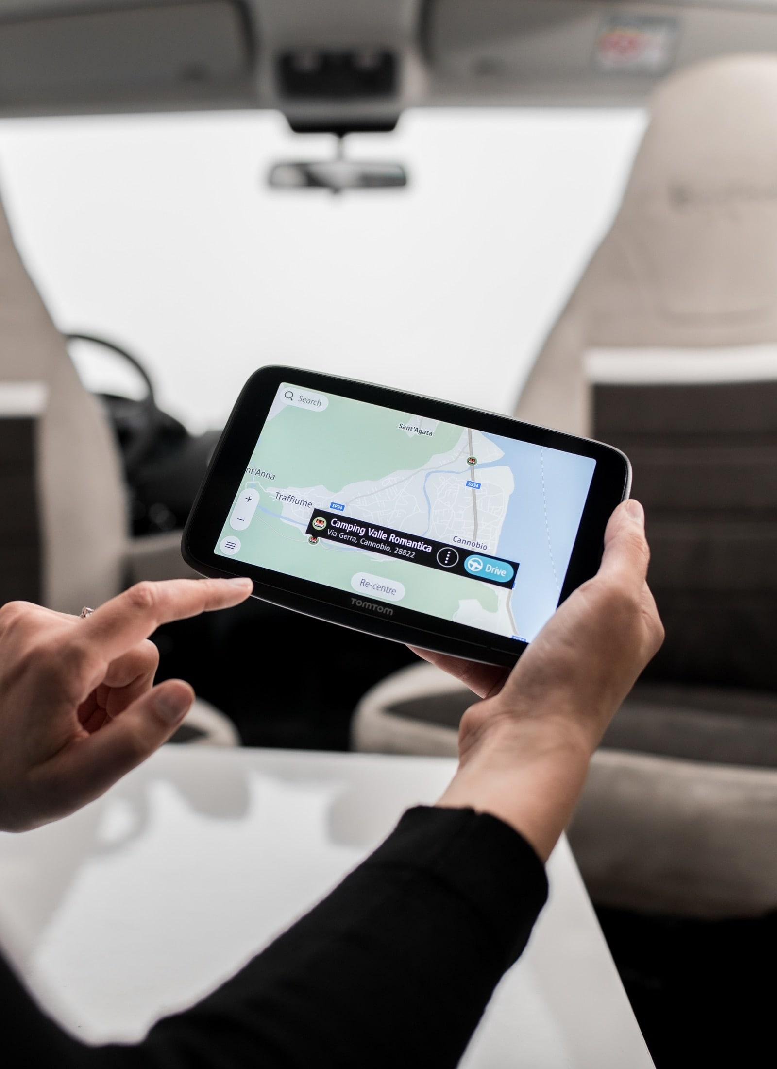 Hände bedienen ein TomTom Navigationsgerät im Auto mit Karte.