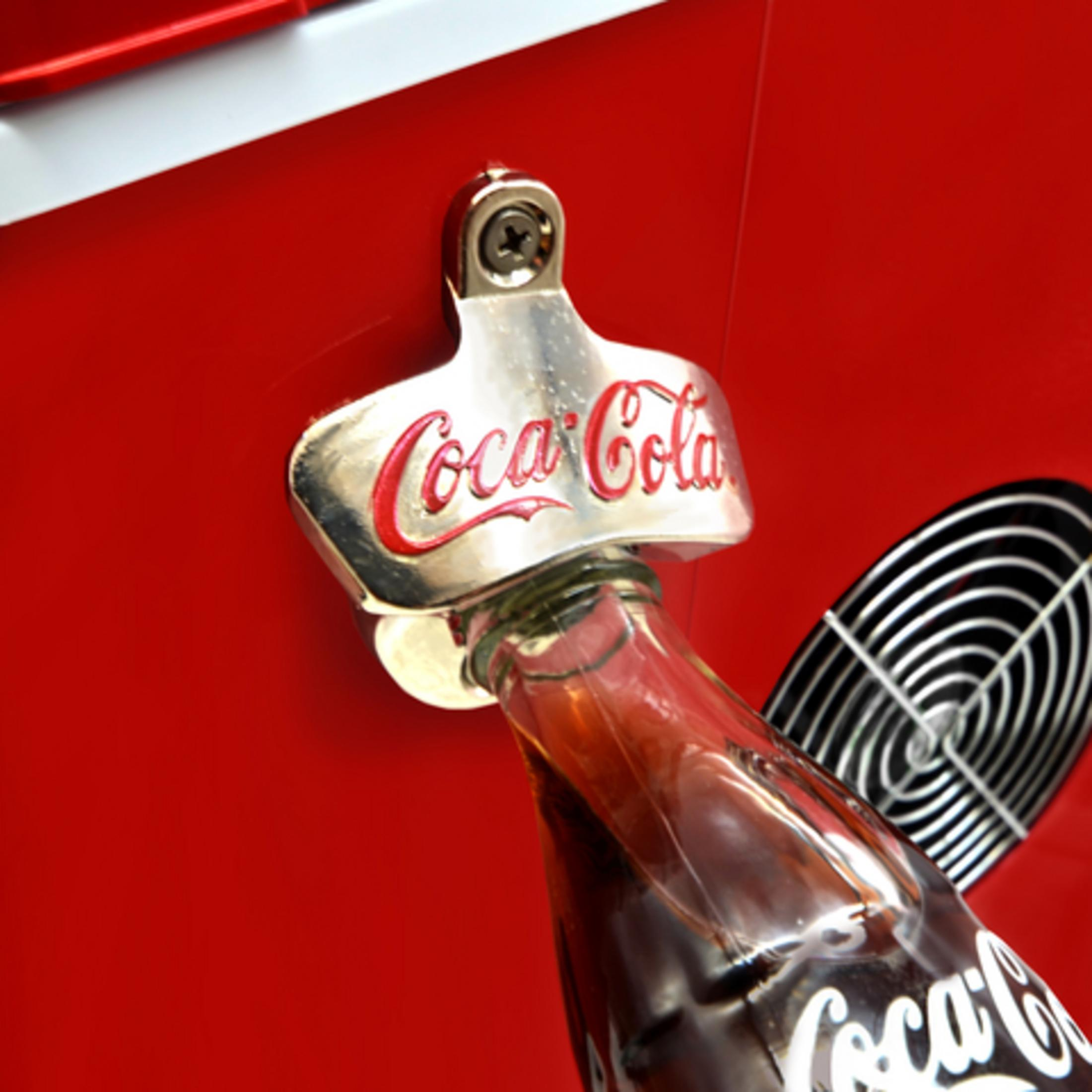 Un apribottiglie Coca-Cola argentato apre una bottiglia di vetro marrone.