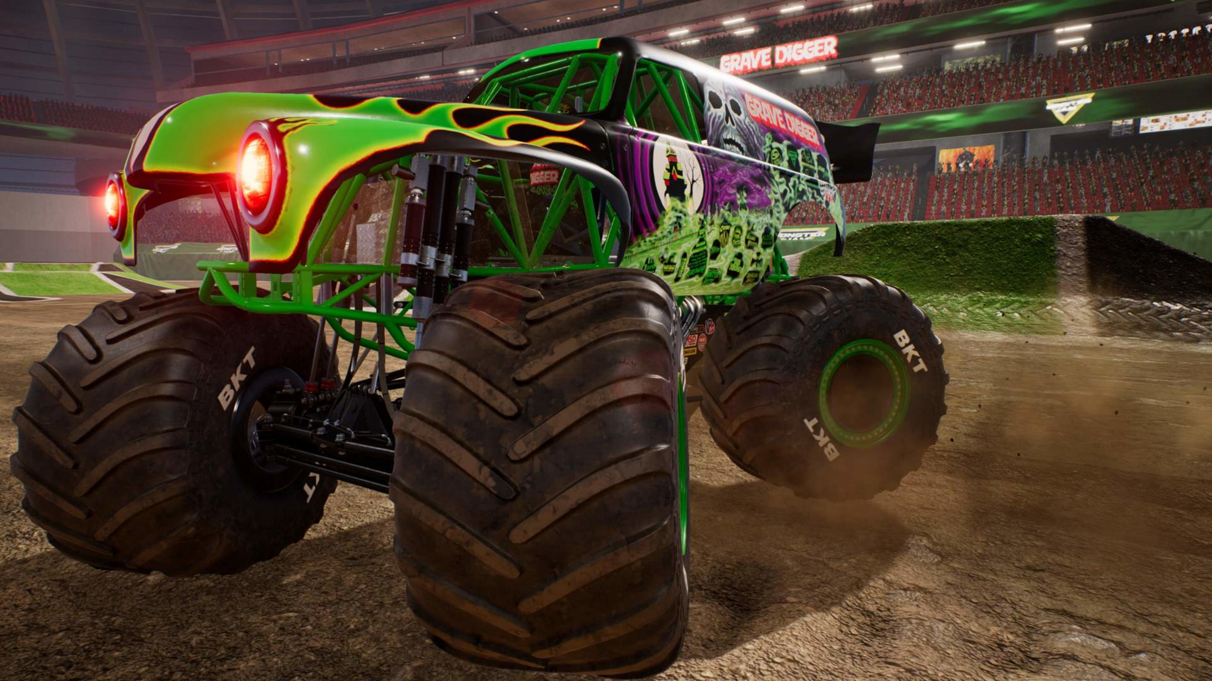 Zielony monster truck z motywem płomieni i czerwonymi światłami w arenie.