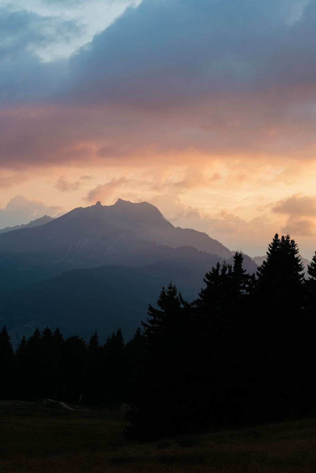 Silhouette of trees and mountains at sunset with orange clouds.