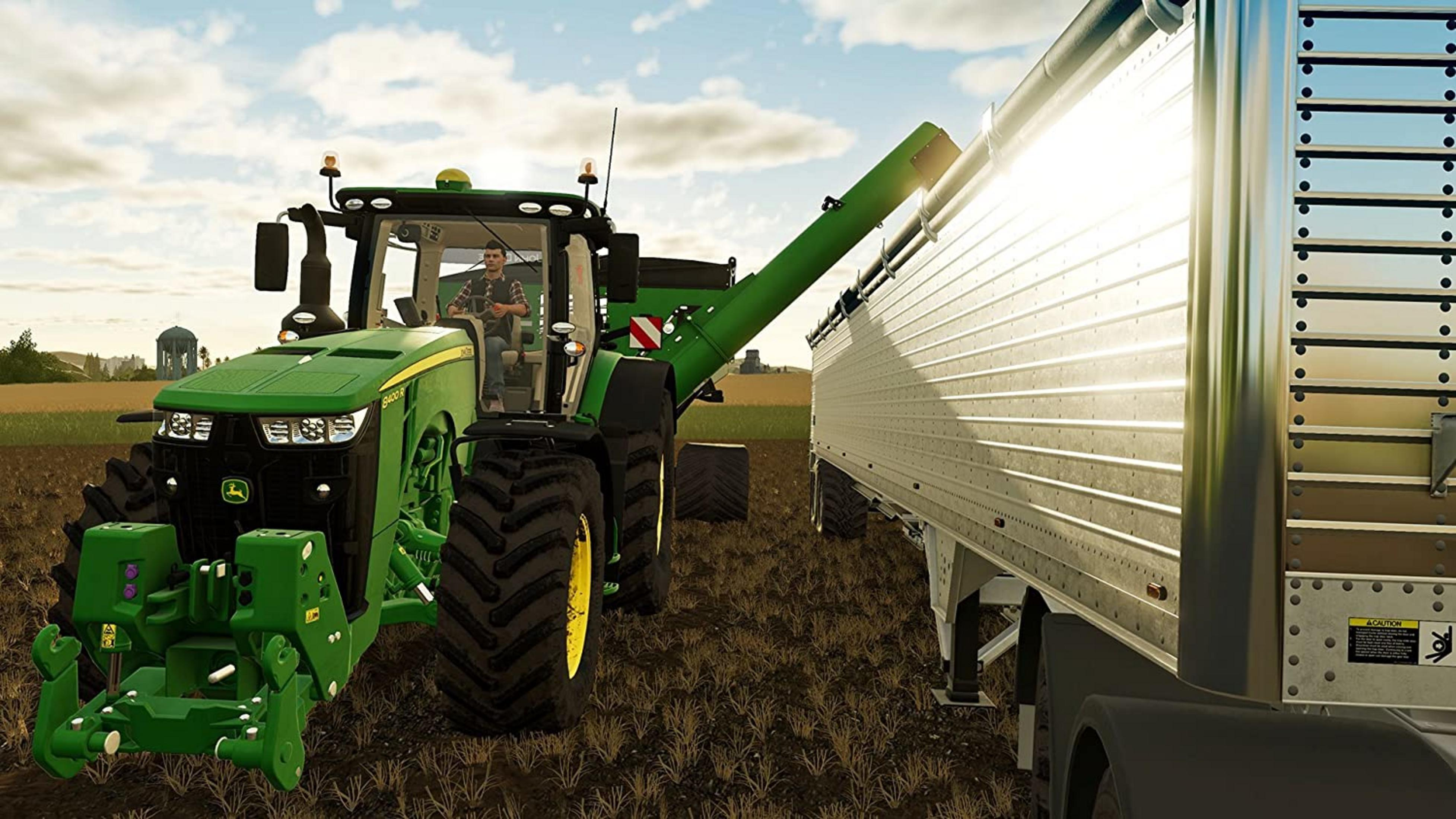 Zielony traktor John Deere z kierowcą ładuje przyczepę przez rurę.