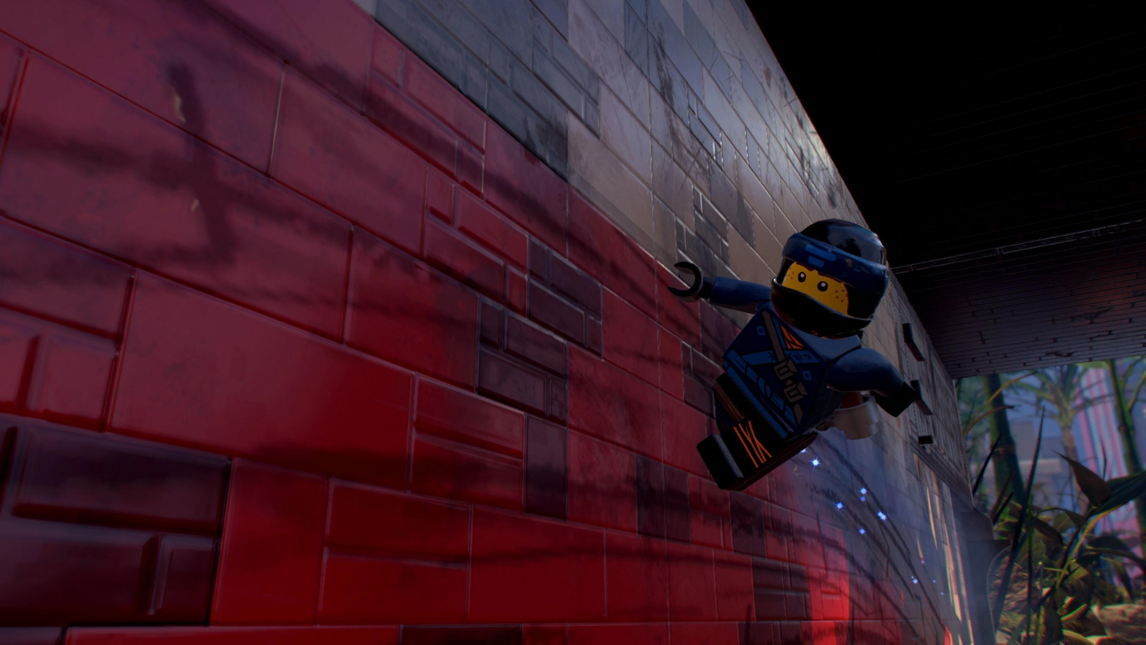 Un personaggio Lego si arrampica su un muro di mattoni rossi. Nel retro si vede fogliame verde.