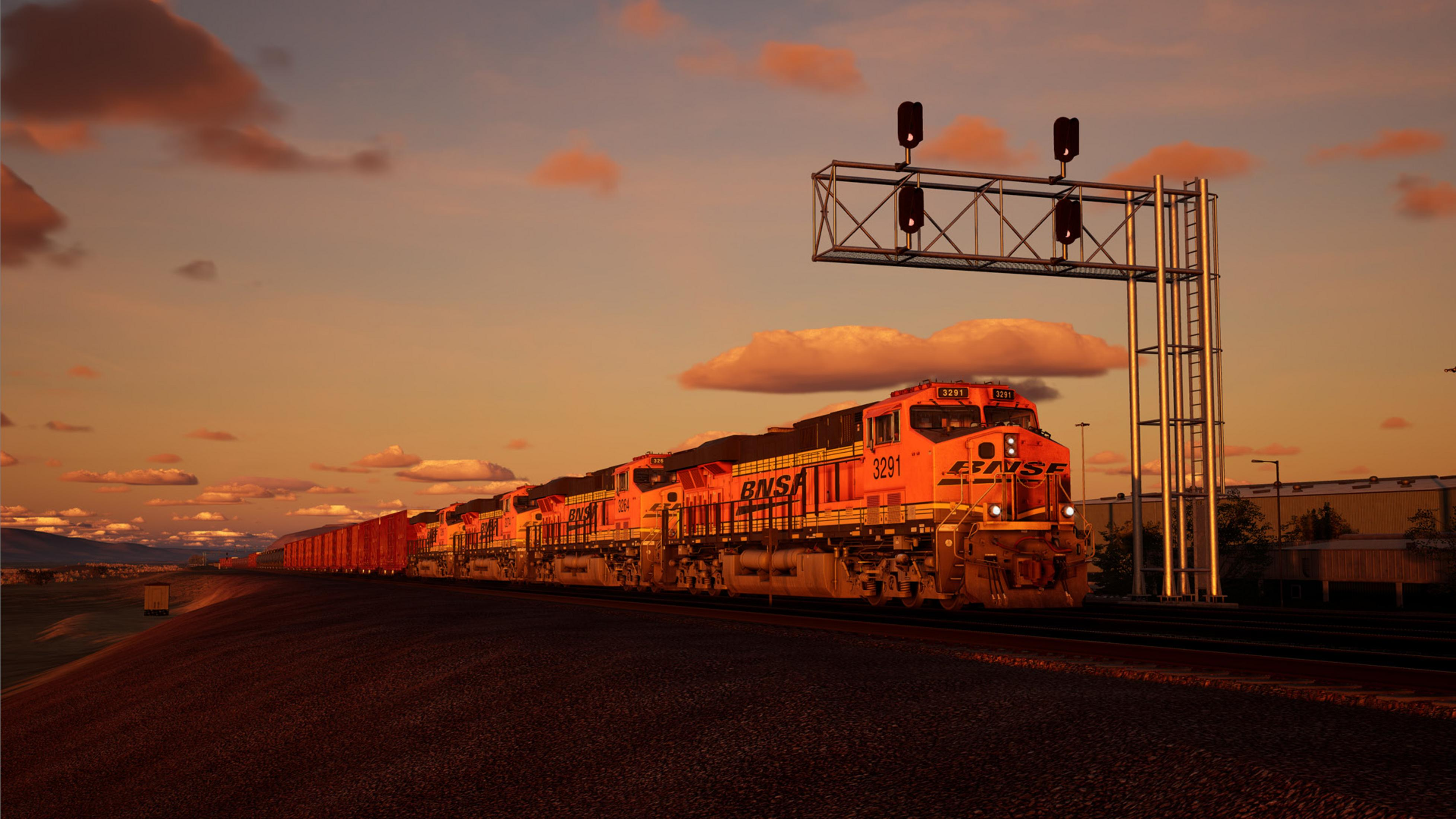 Eine orangefarbene BNSF-Lokomotive fährt bei Sonnenuntergang neben einem Güterzug.