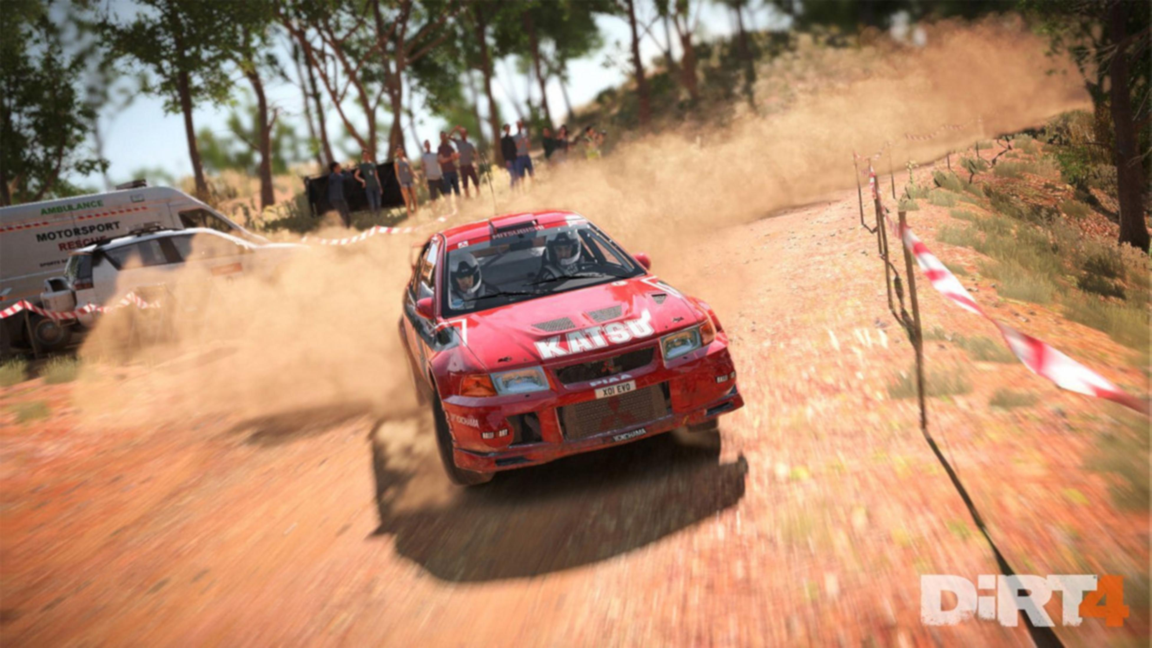 Ein rotes Rallyeauto fährt auf einer staubigen Strecke, begleitet von einem Krankenwagen.