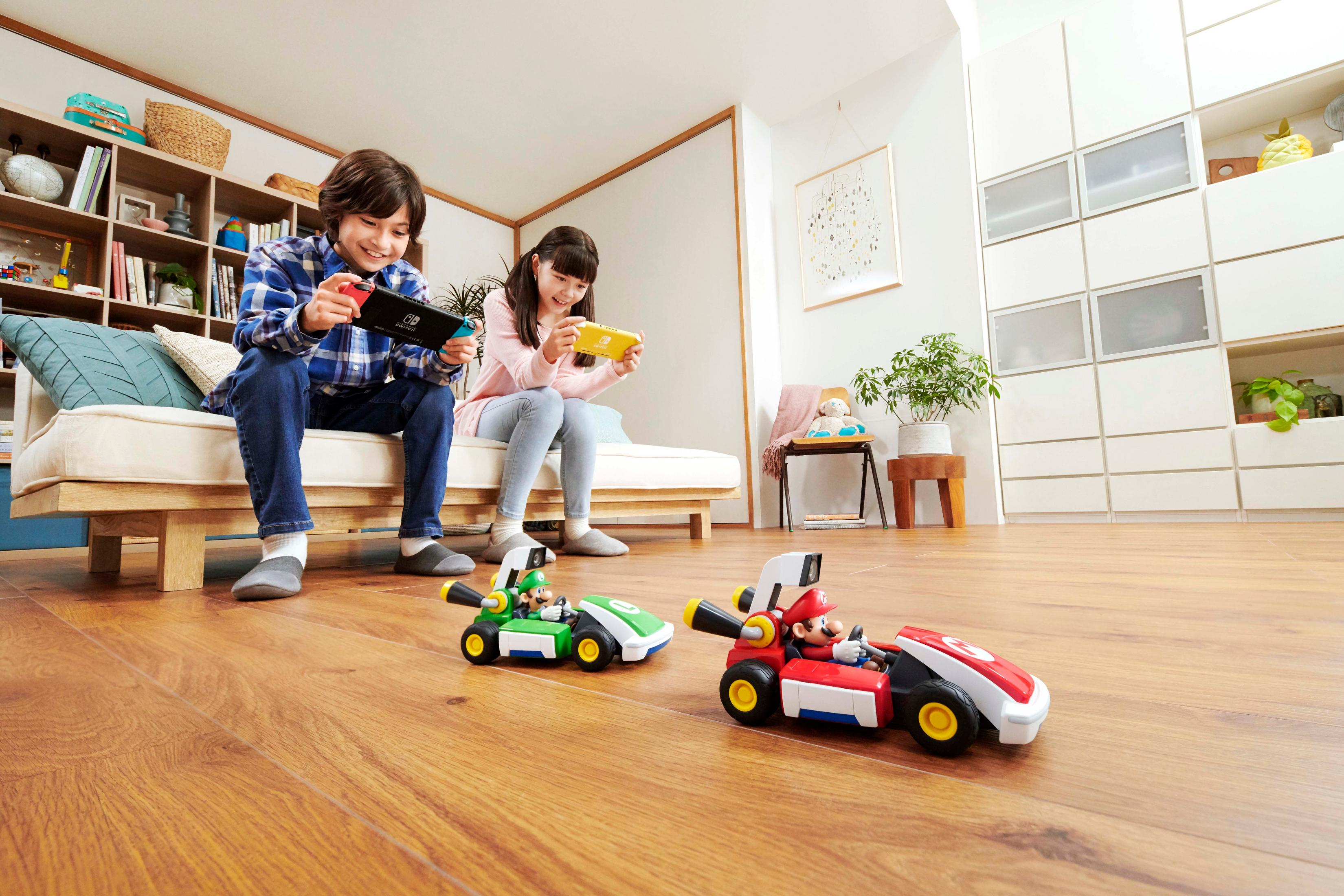 Zwei Kinder spielen auf einem Sofa Nintendo Switch. Mario und Luigi fahren ferngesteuerte Go-Karts.
