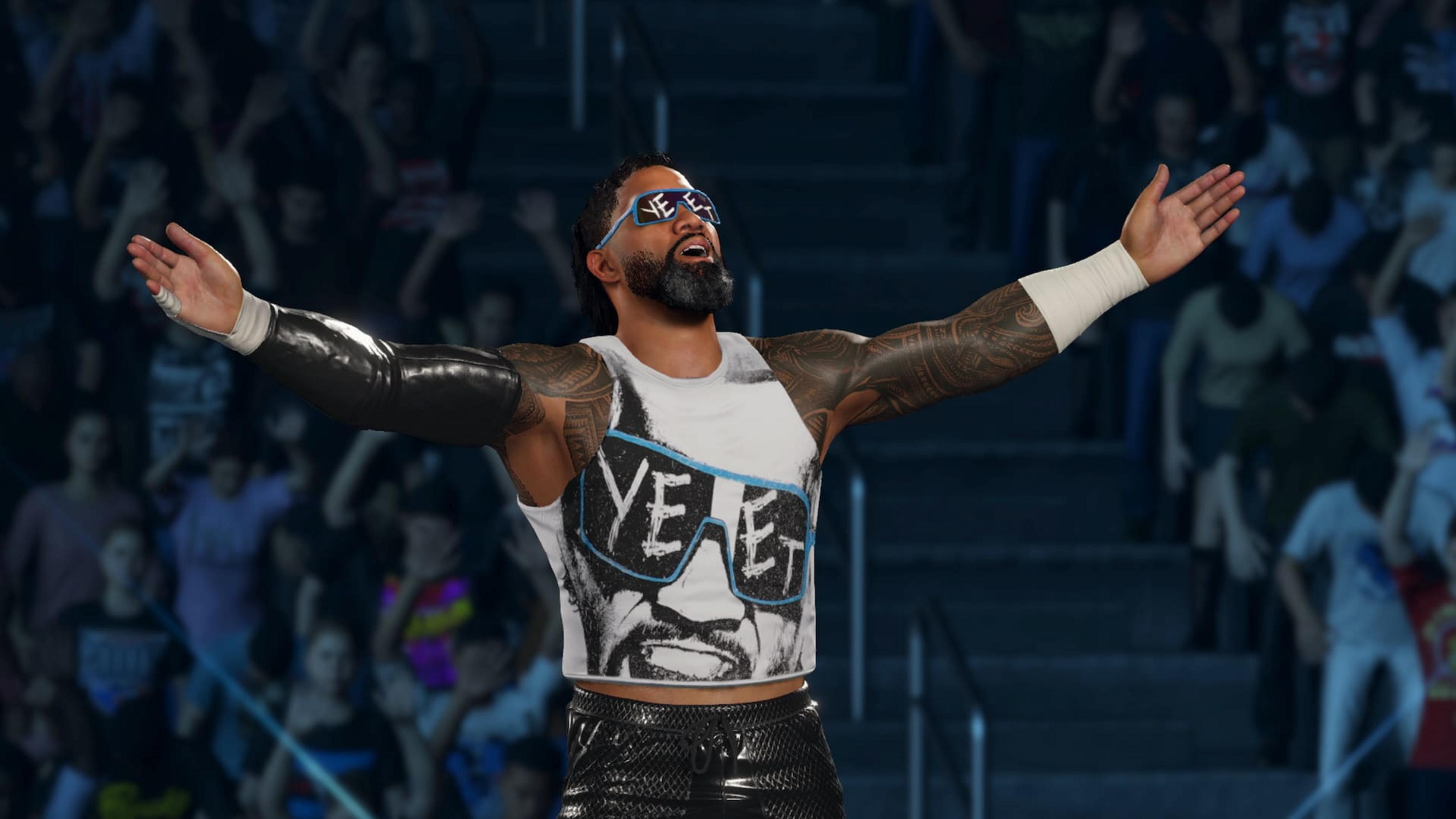 Ein Wrestler mit Tätowierungen und Sonnenbrille steht mit ausgebreiteten Armen vor einem Publikum.