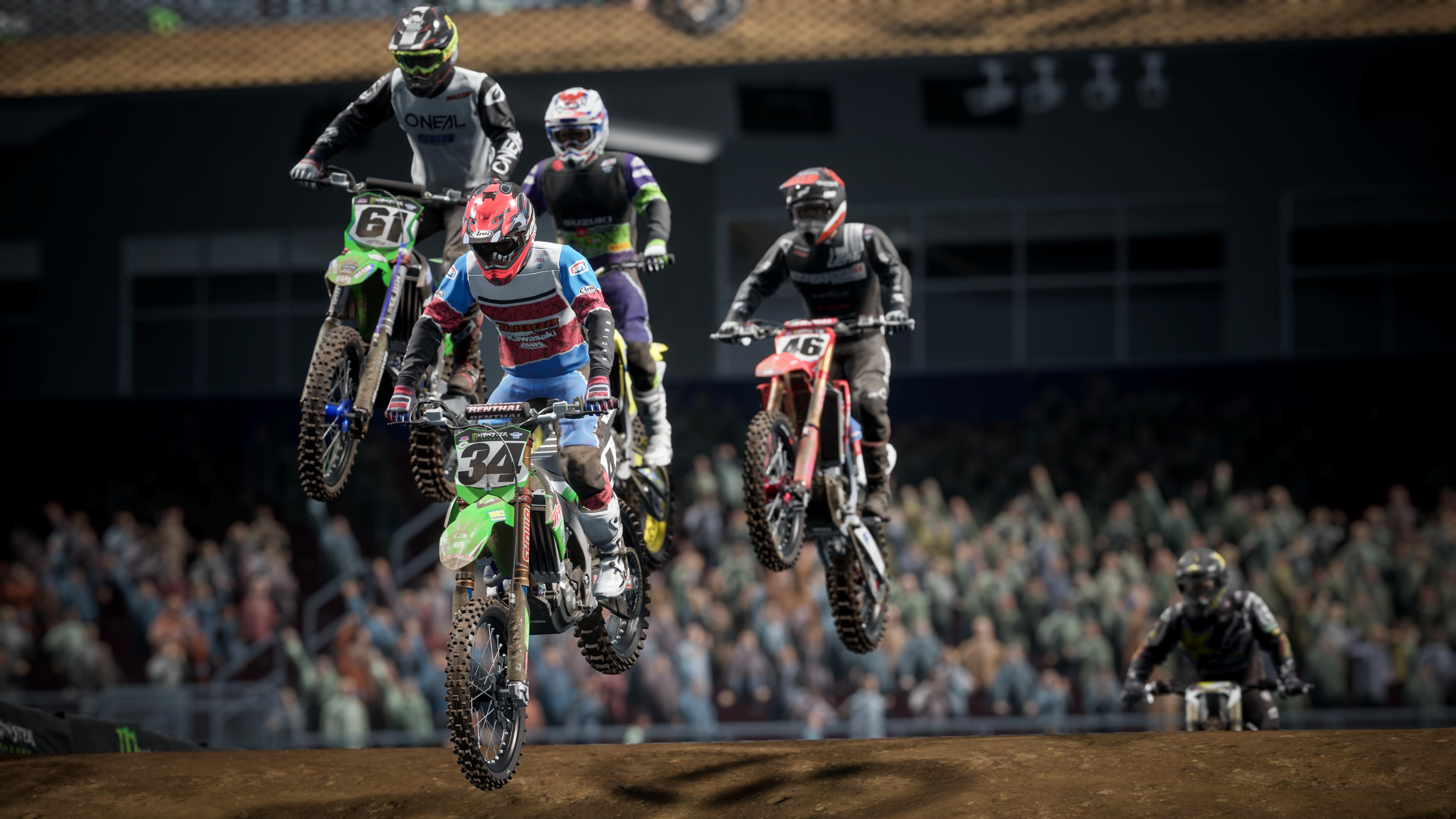 Motocross-Fahrer springen über eine Schmutzrampe vor einem Stadionpublikum.