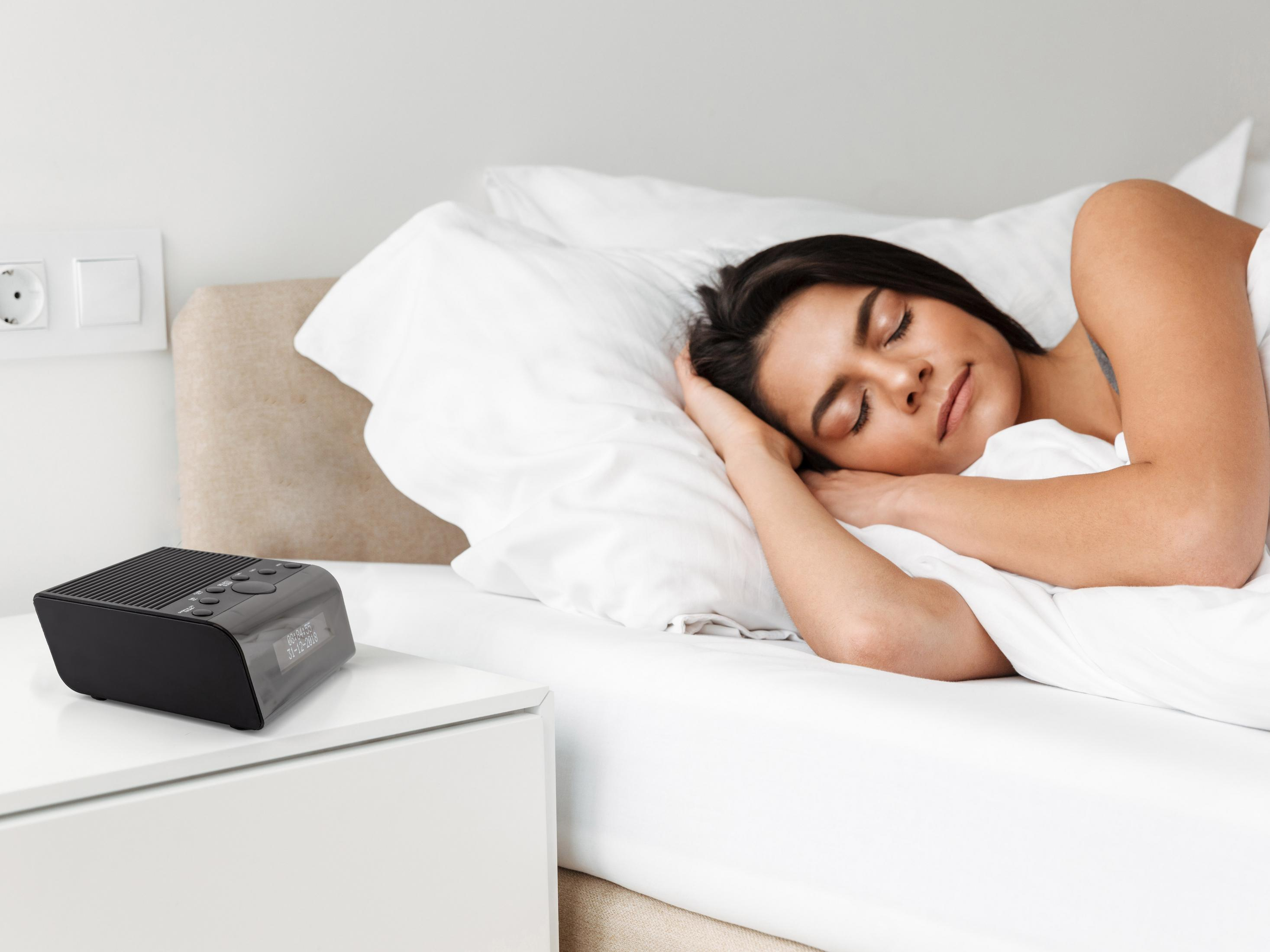 Une femme dort dans un lit à côté d'une table de chevet avec radio-réveil.
