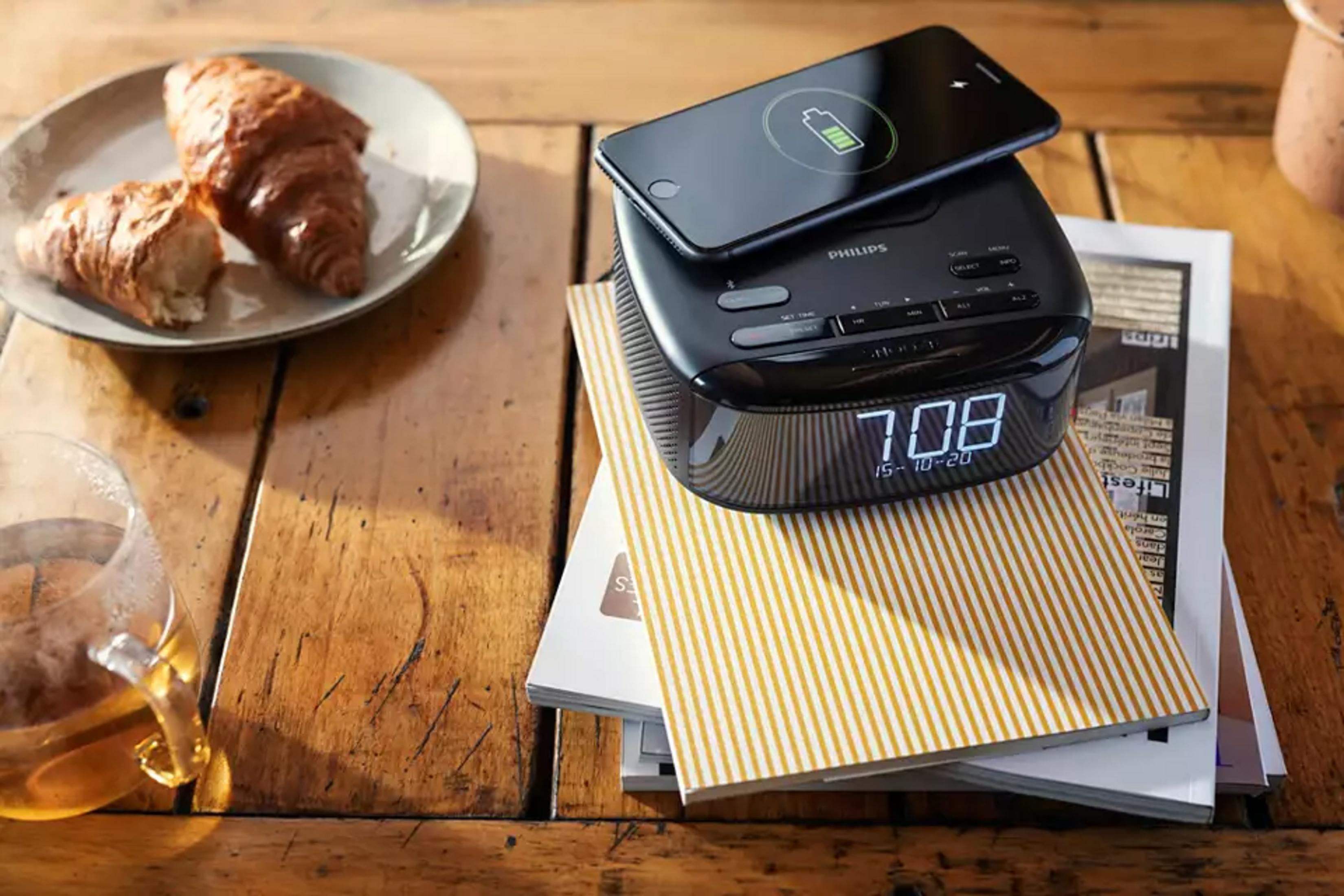 Budzik Philips z ładowarką do telefonu, croissantami i herbatą na drewnianym stole.