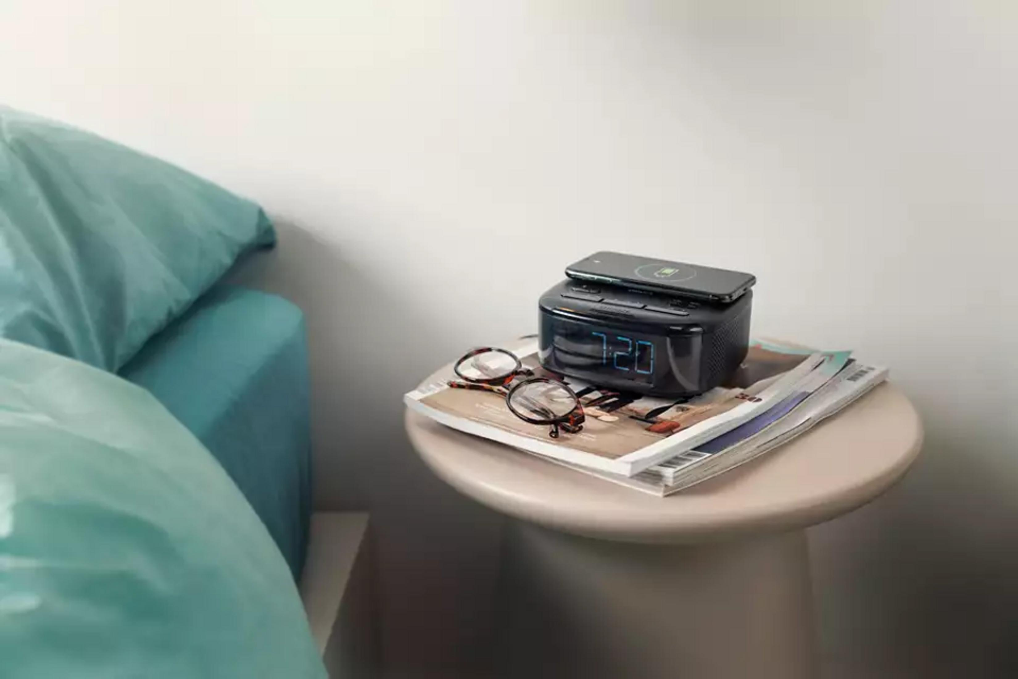 Zegarek cyfrowy z telefonem i okularami na magazynach obok łóżka.