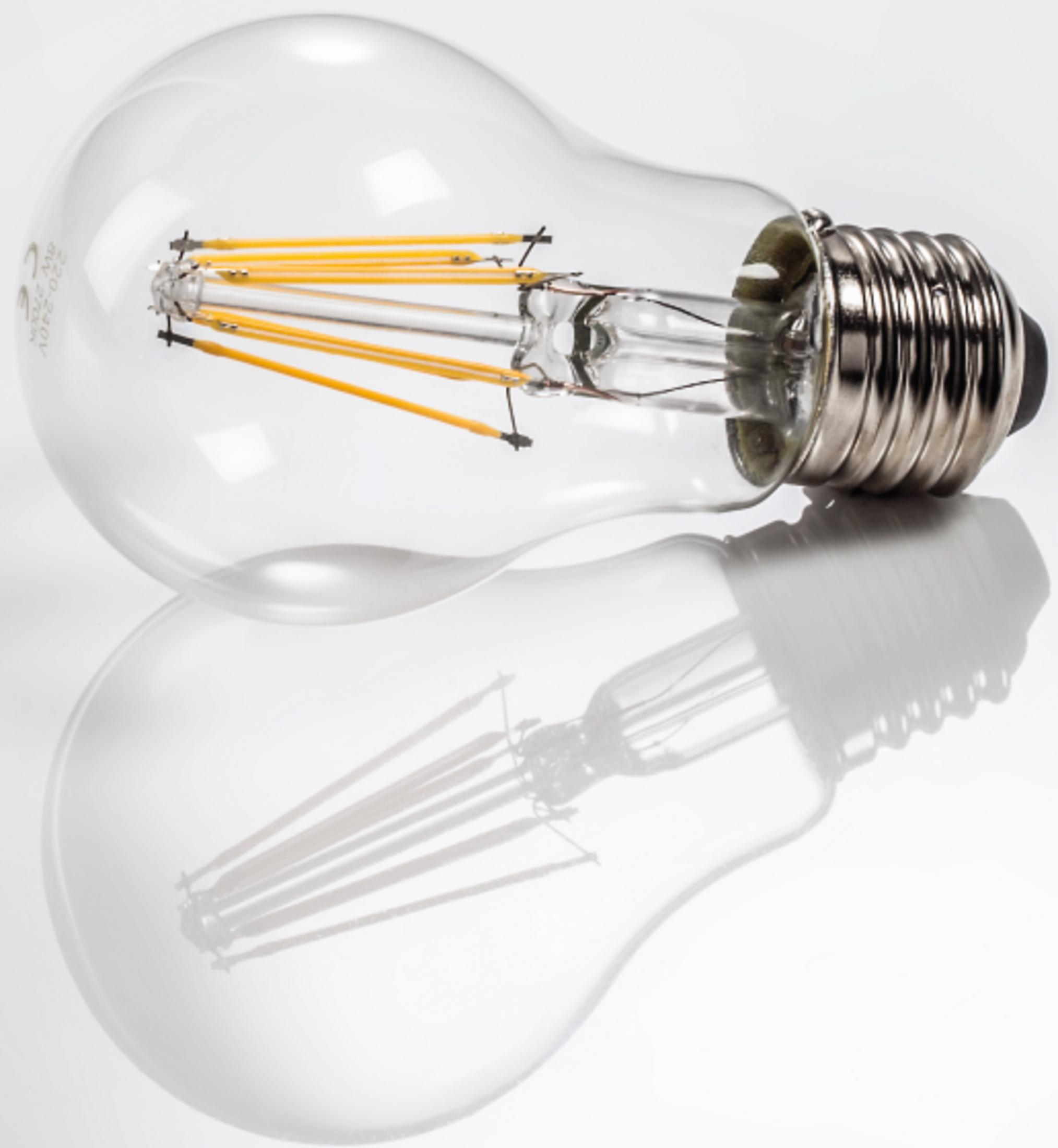Przezroczysta żarówka z żółtymi żarnikami leży na białej, odblaskowej powierzchni.
