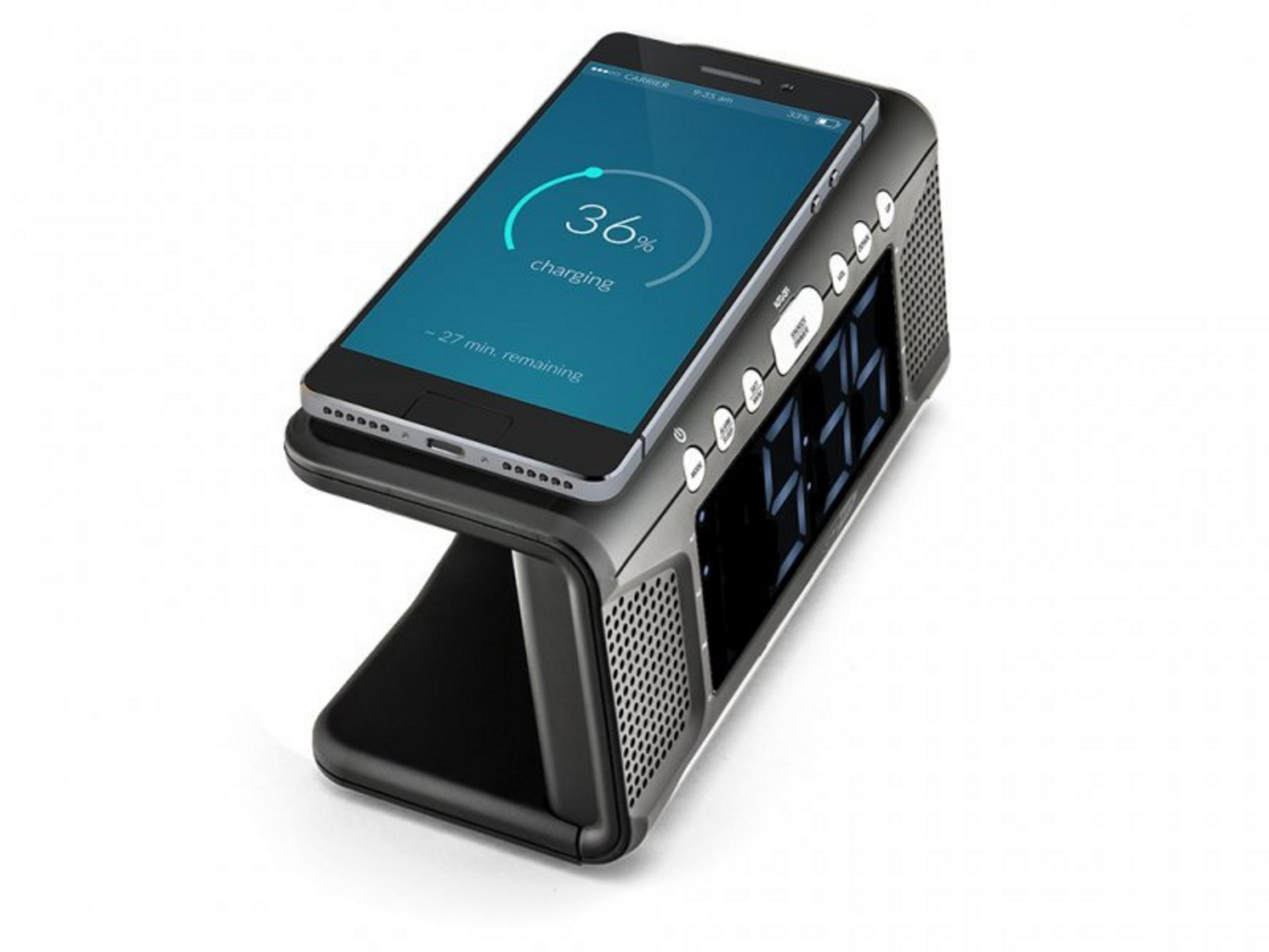 A black alarm clock with charging function. A smartphone is charging.