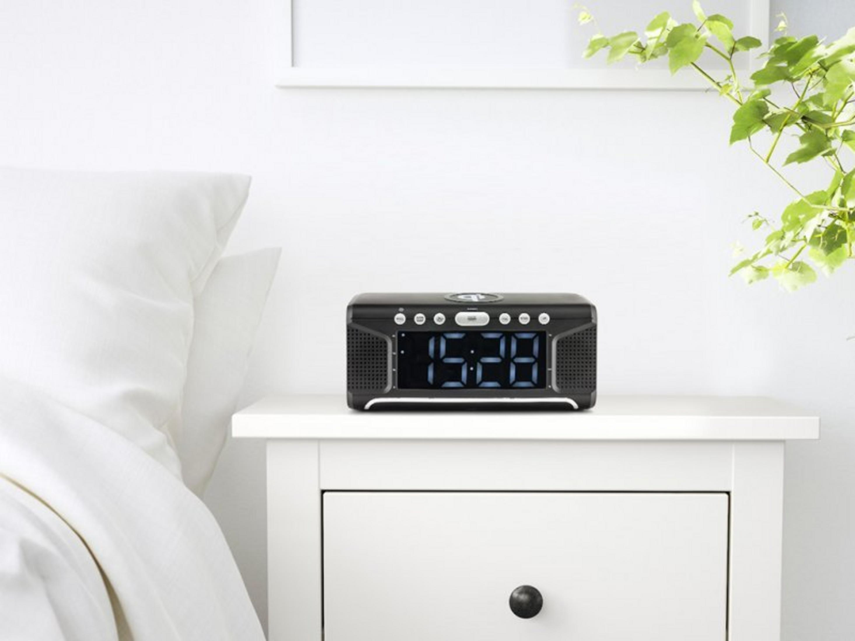 Black digital alarm clock with blue display on nightstand next to bed.