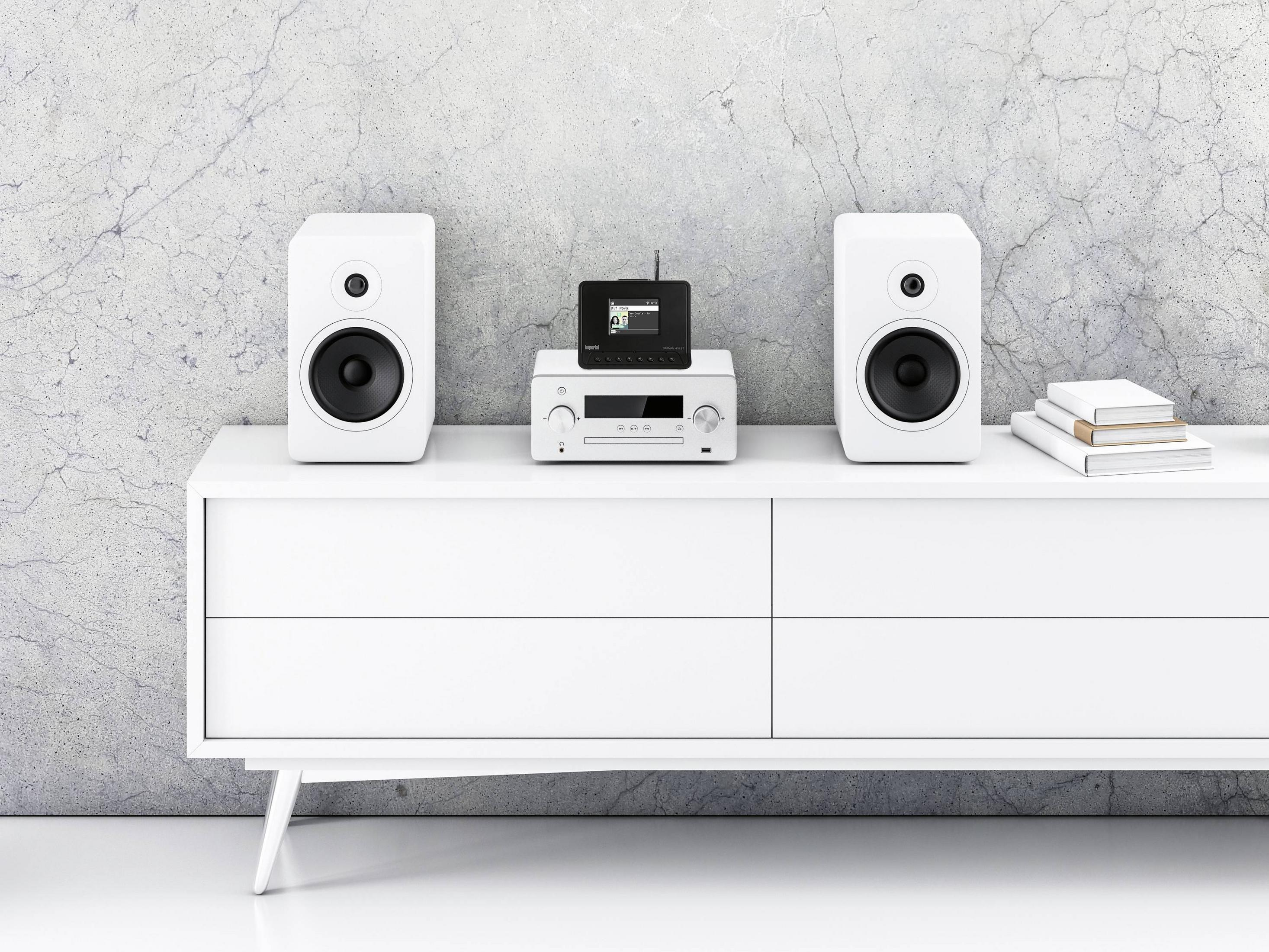 Dwa białe głośniki flankują srebrny system audio z czarnym wyświetlaczem.