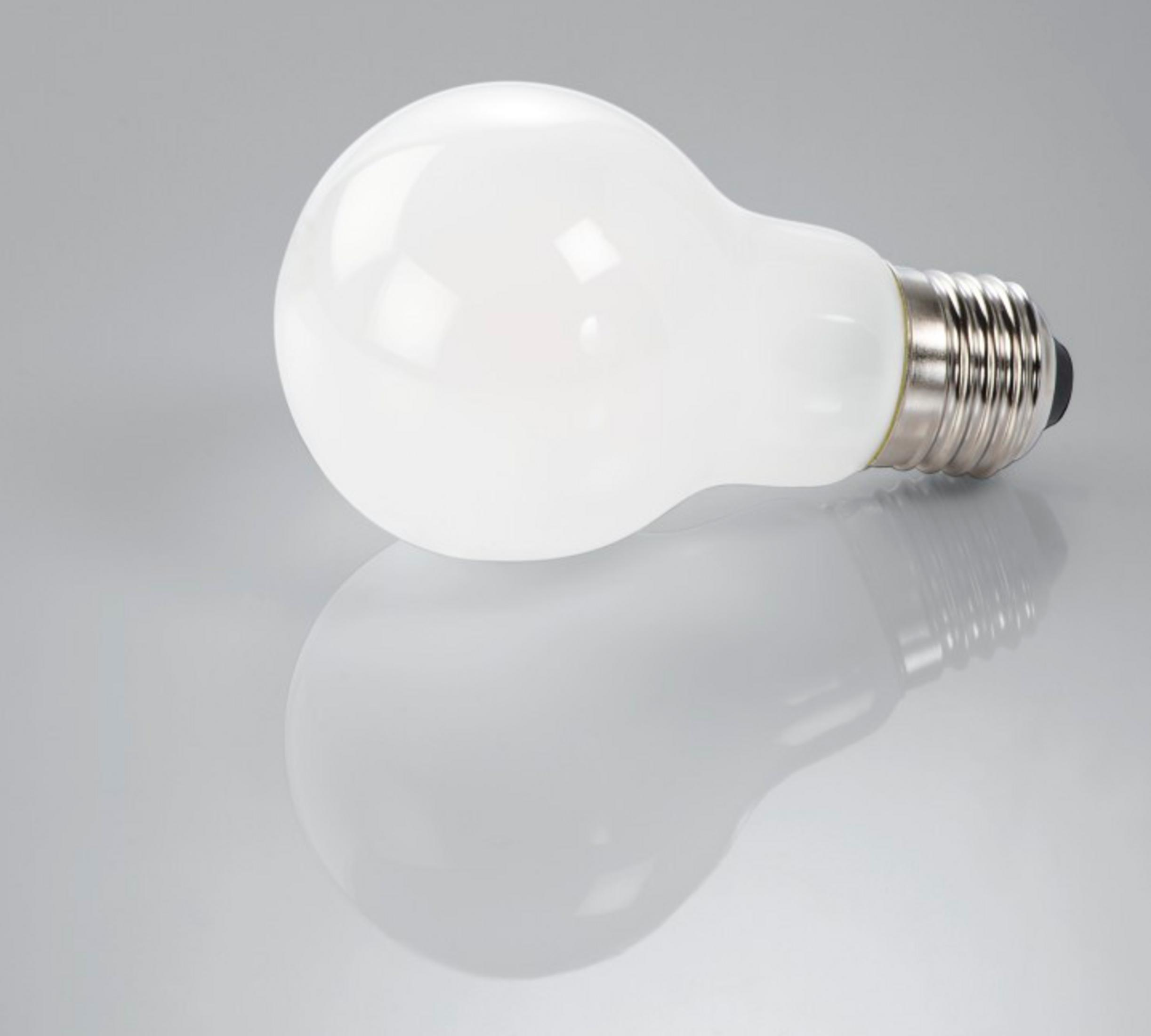 Biała żarówka leży na odblaskowej powierzchni.