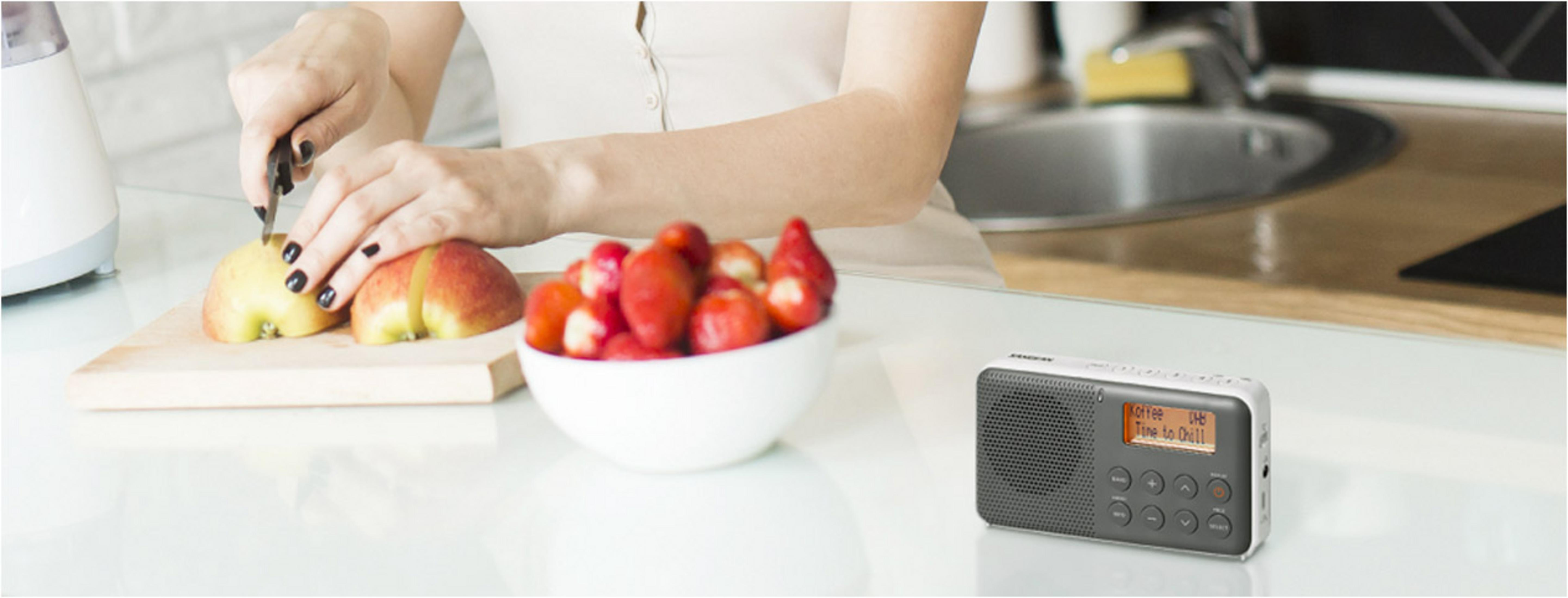 Kobieta kroi jabłko, obok miski truskawek i radia.