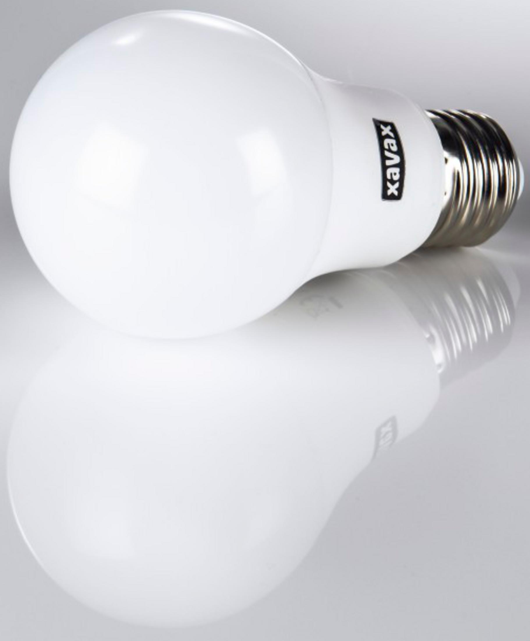 Una lampadina a LED bianca con base a vite argentata poggia su una superficie riflettente.