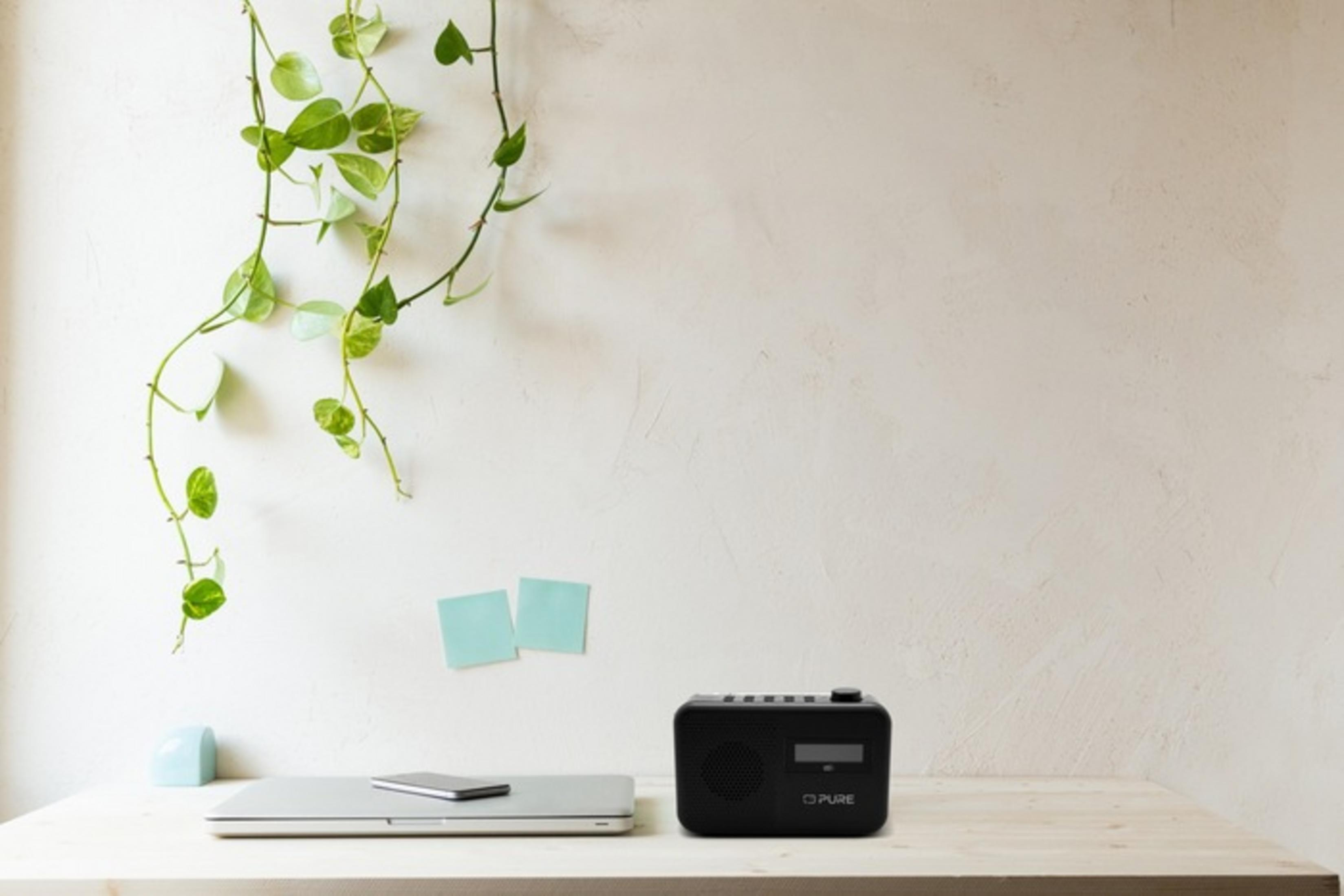 Czarno DAB radio stoi na biurku obok laptopa i rośliny.