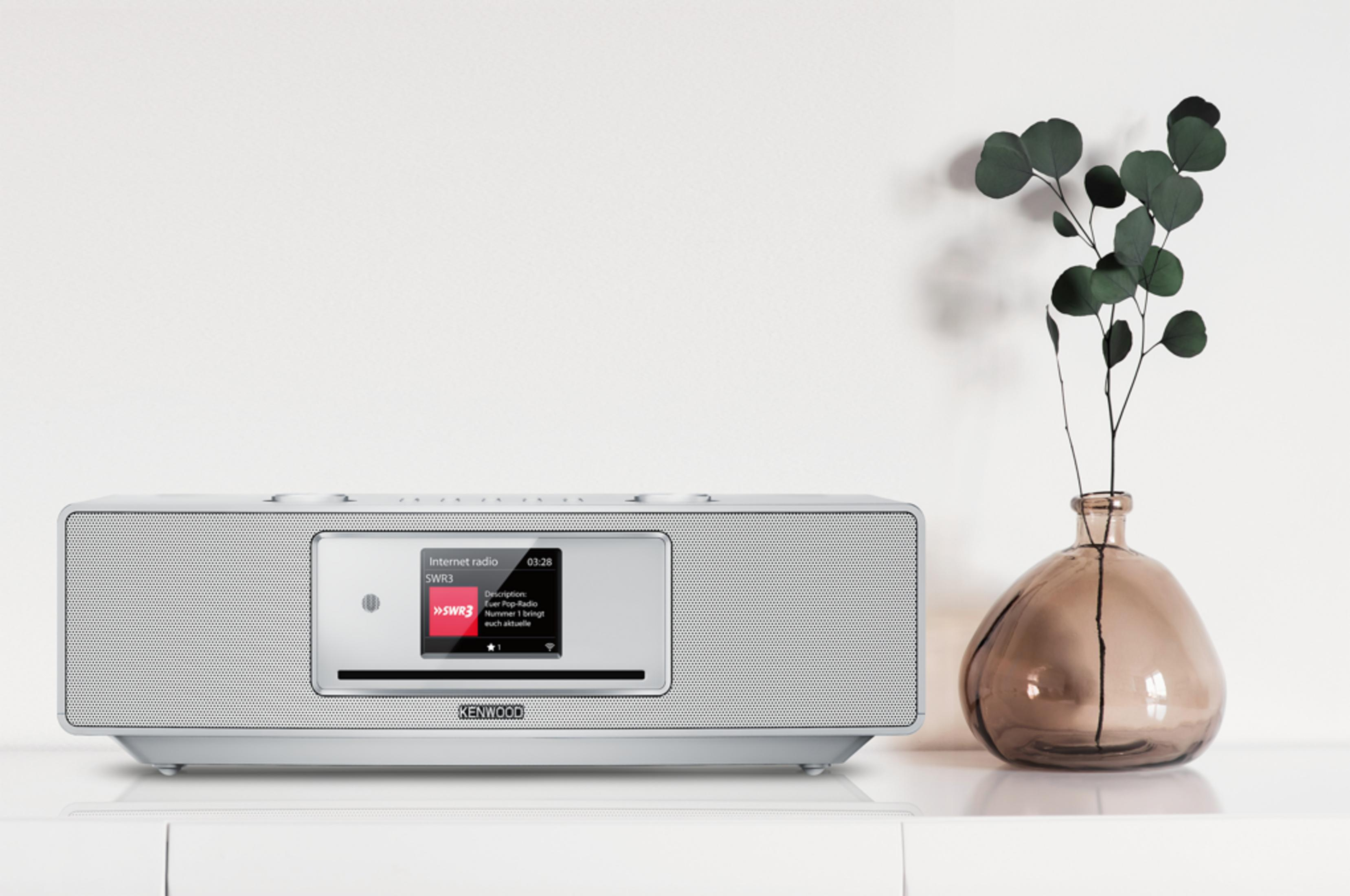 Une radio internet Kenwood argentée sur une étagère avec un vase et des branches.