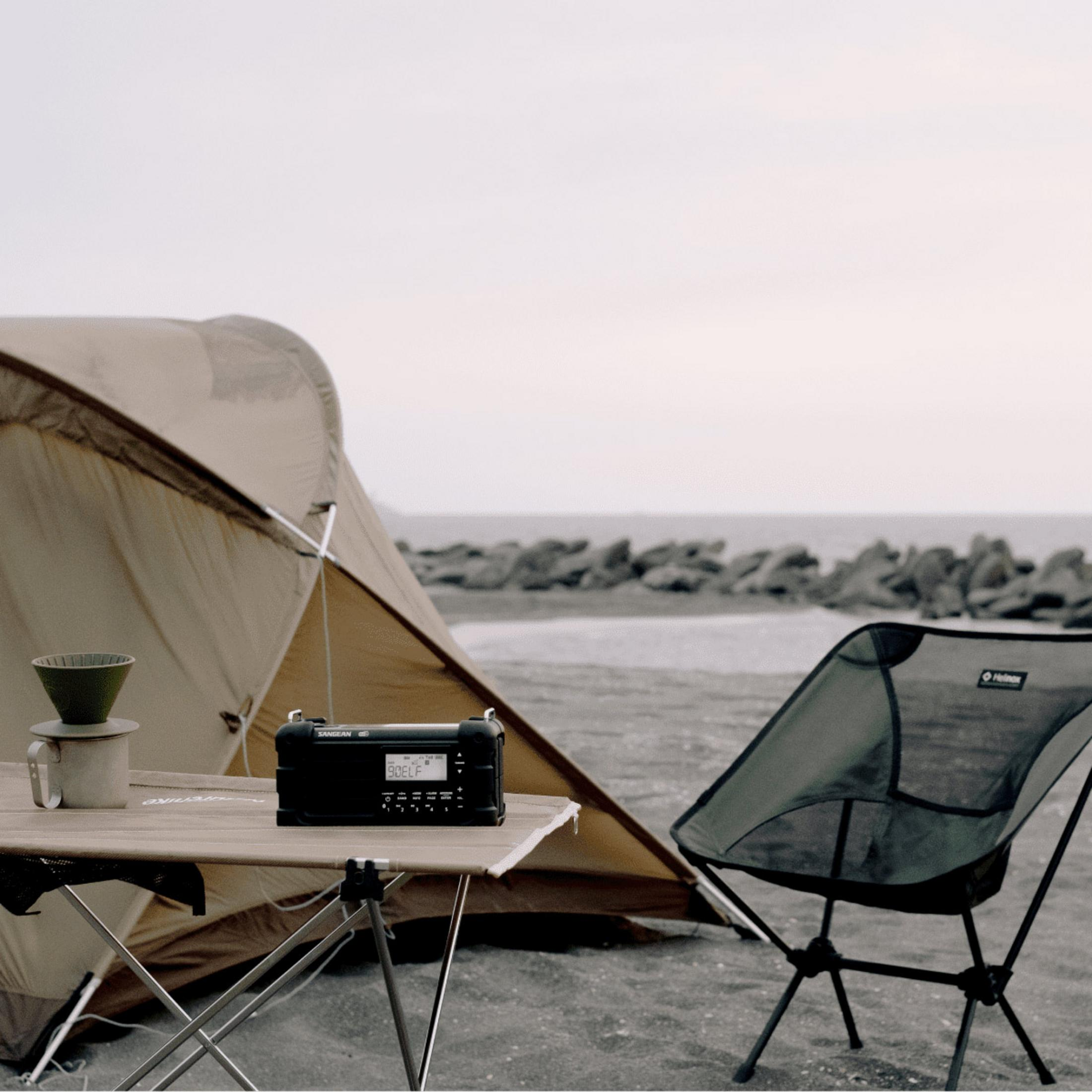 Ein Radio und ein Stuhl stehen auf einem Tisch vor einem Zelt am Strand.
