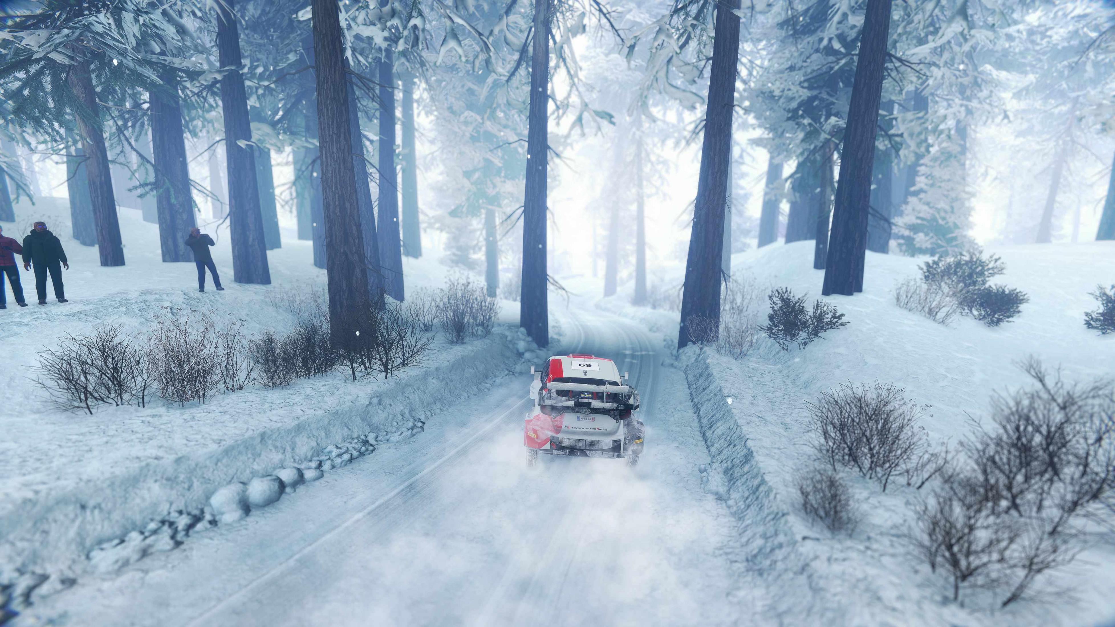Ein roter Rallye-Wagen fährt auf verschneiter Straße durch einen Wald.