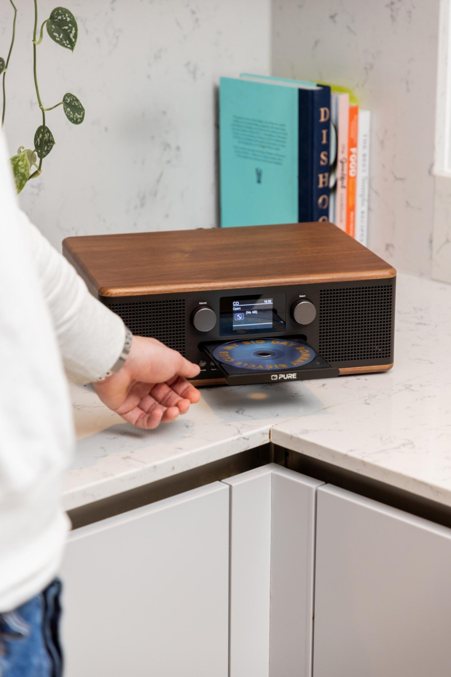 Ręka wkłada płytę CD do drewnianego radia na blacie kuchennym.