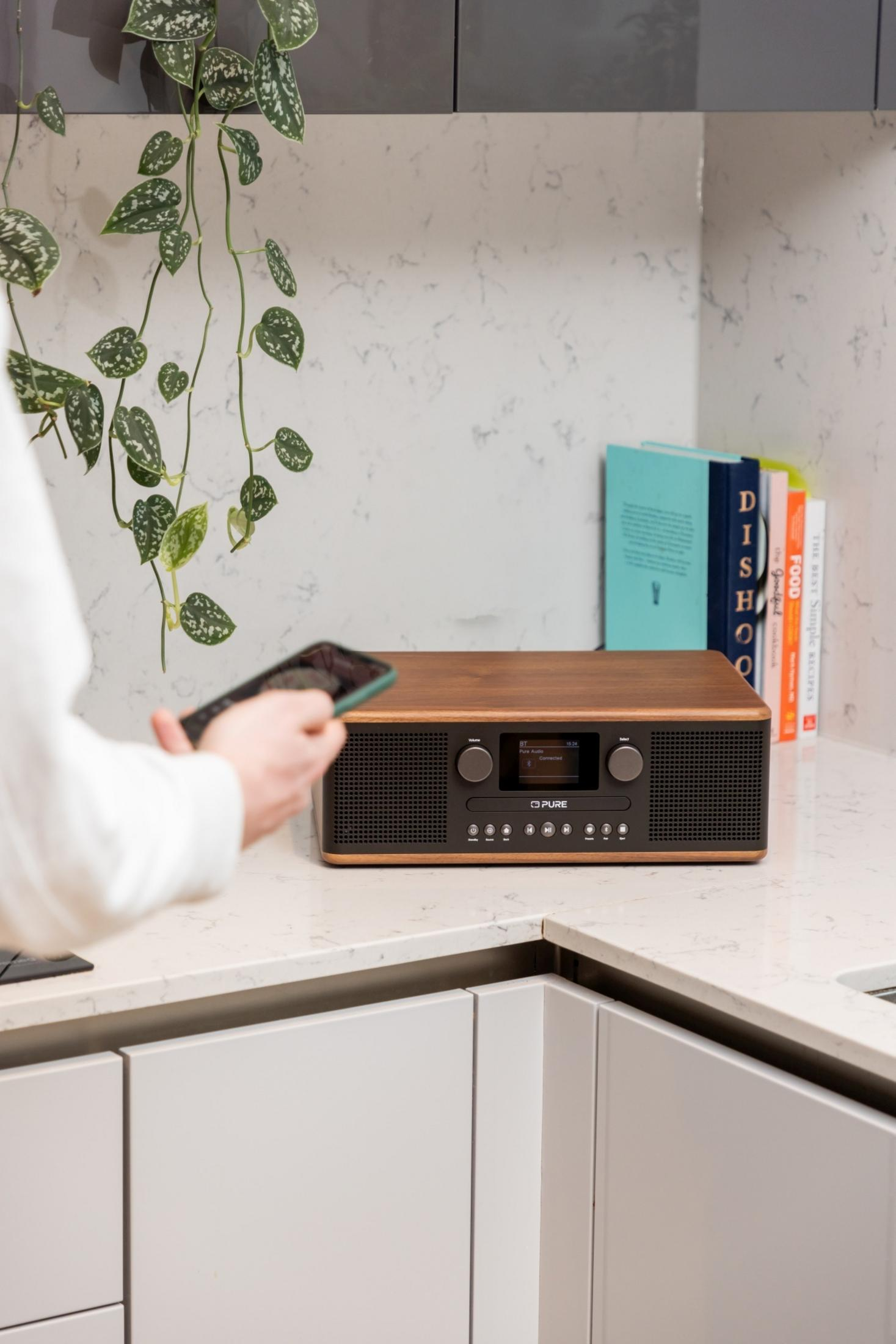 Ręka trzyma smartfona przed drewnianym radiem z ekranem.