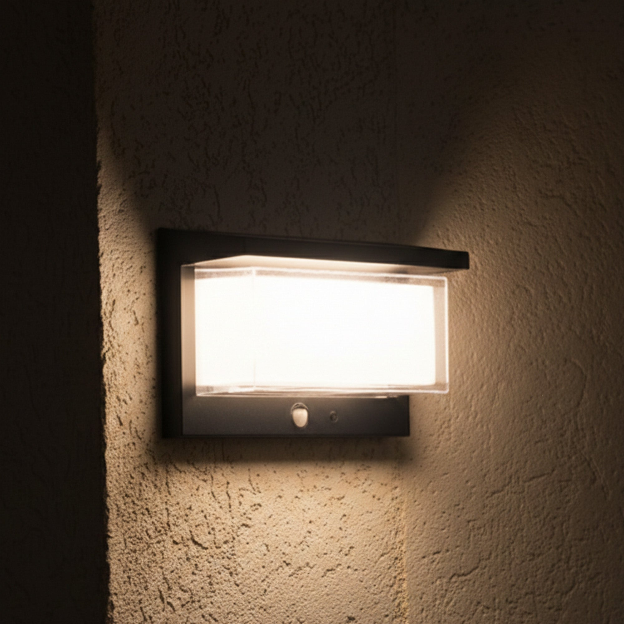 Eine rechteckige Wandleuchte mit schwarzem Rahmen leuchtet hell auf einer strukturierten Wand.