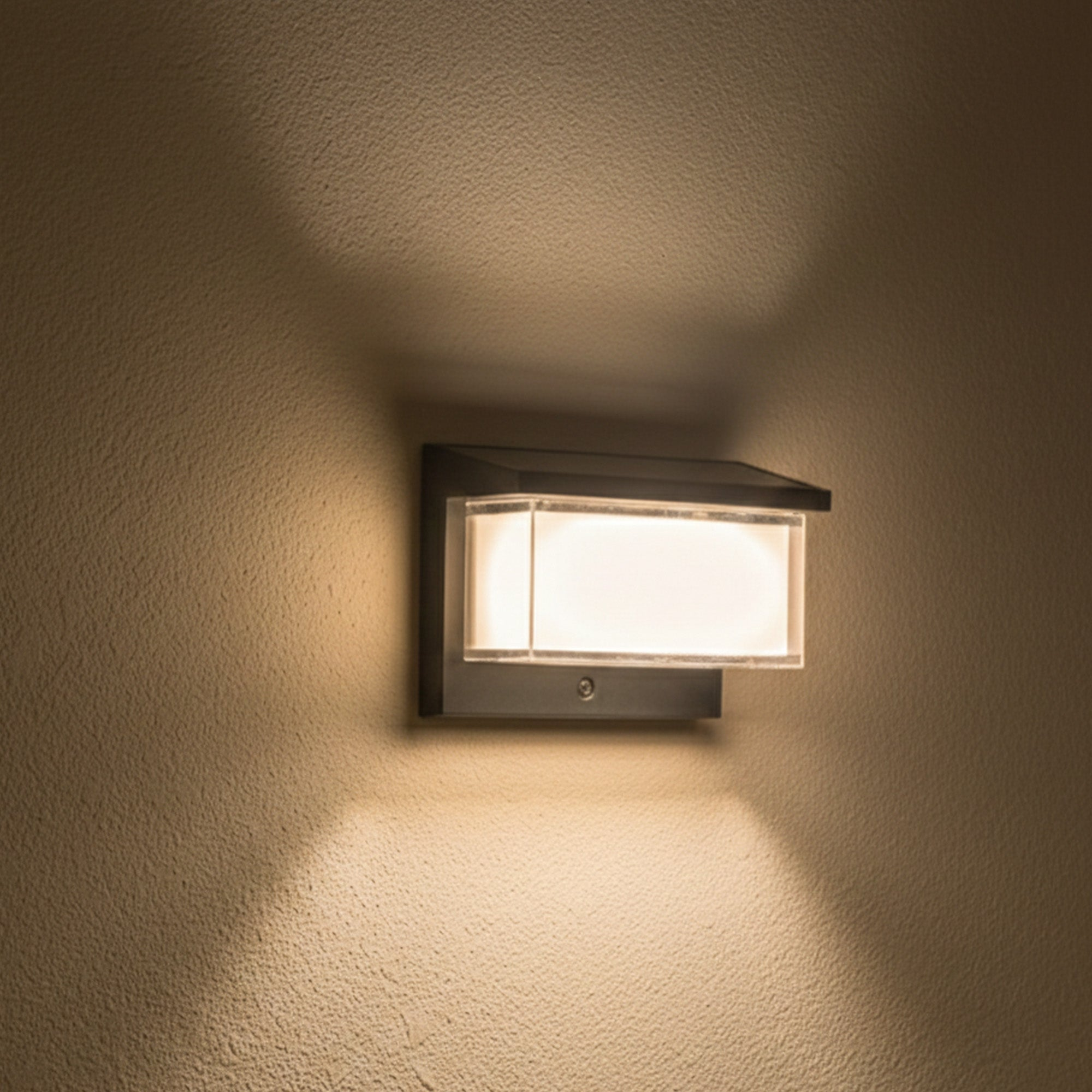 Eine rechteckige Wandleuchte mit Glasfront leuchtet hell an einer strukturierten Wand.