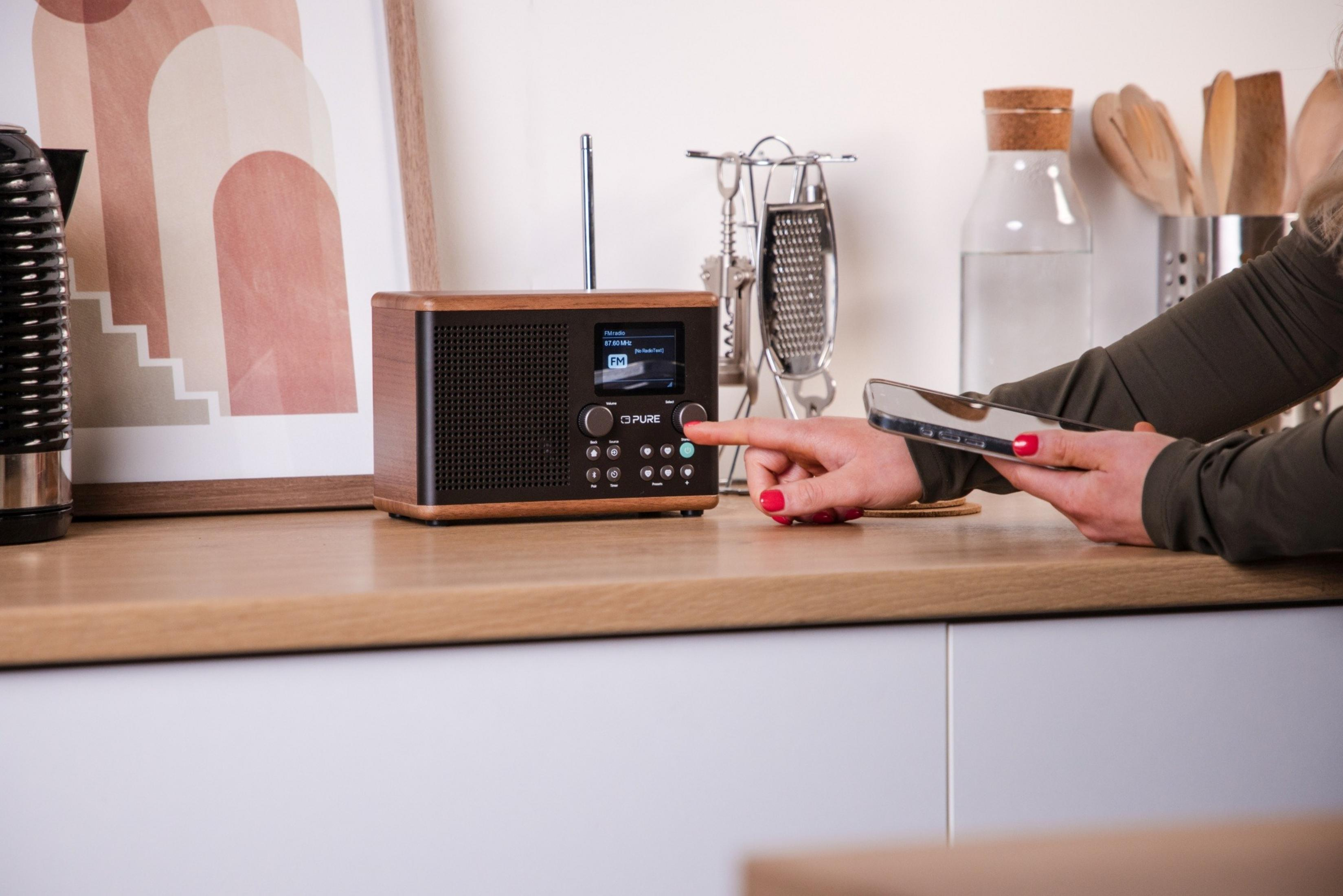 Osoba obsługuje palcem drewniane radio, trzymając smartfon.