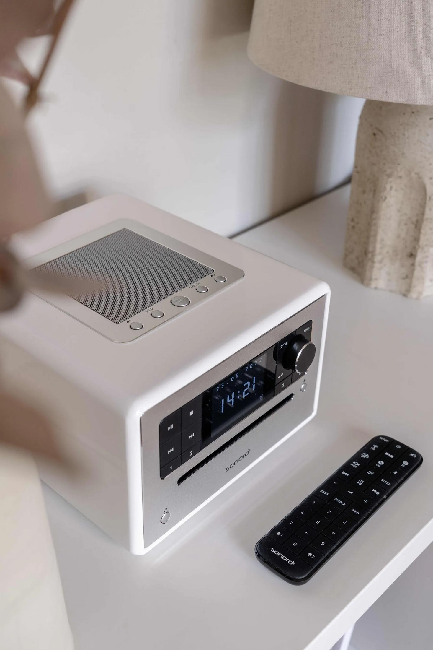 Een witte radio met afstandsbediening op een witte tafel.