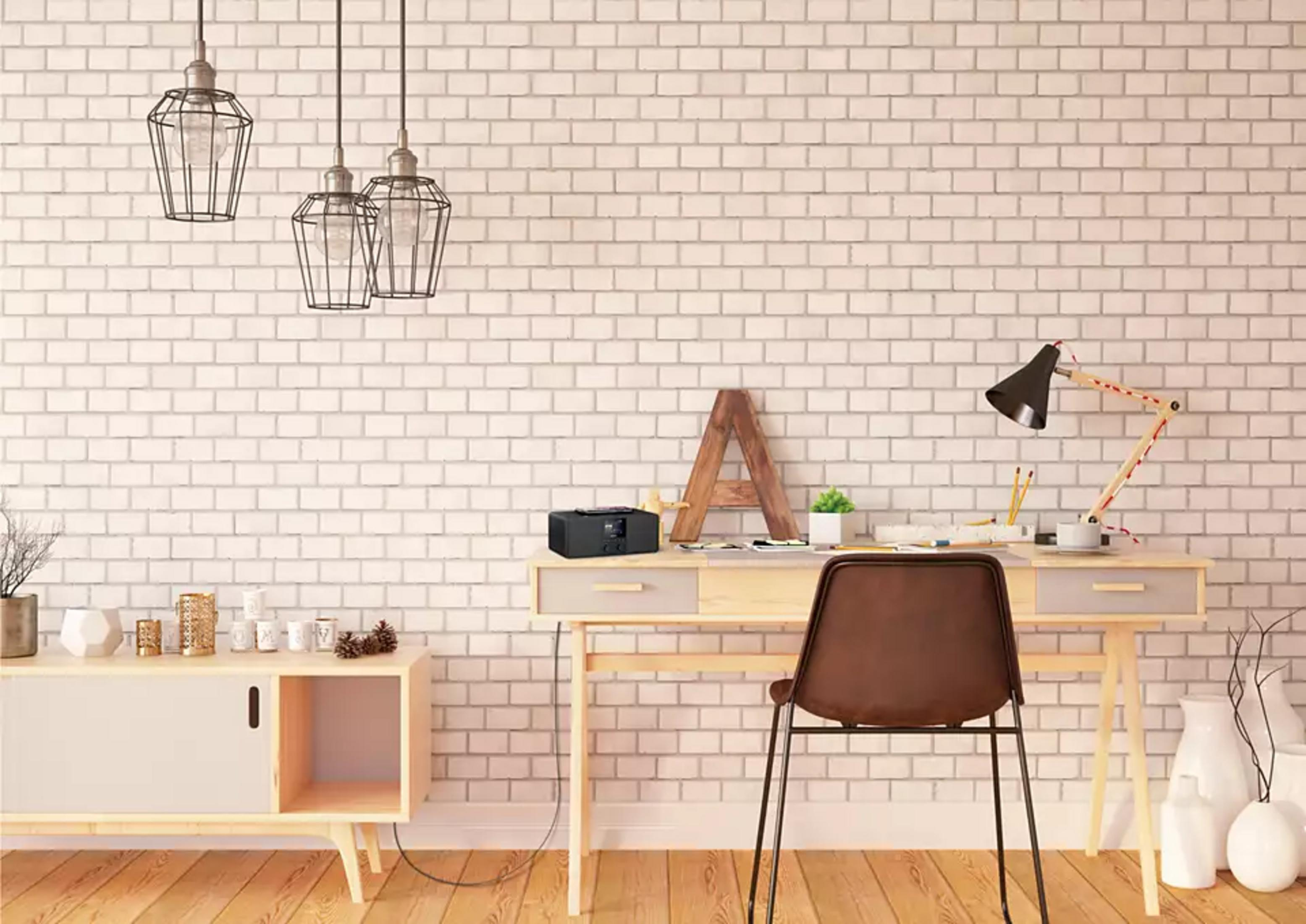 Ein Schreibtisch mit Lampe, Stuhl und Radio vor einer Backsteinwand.