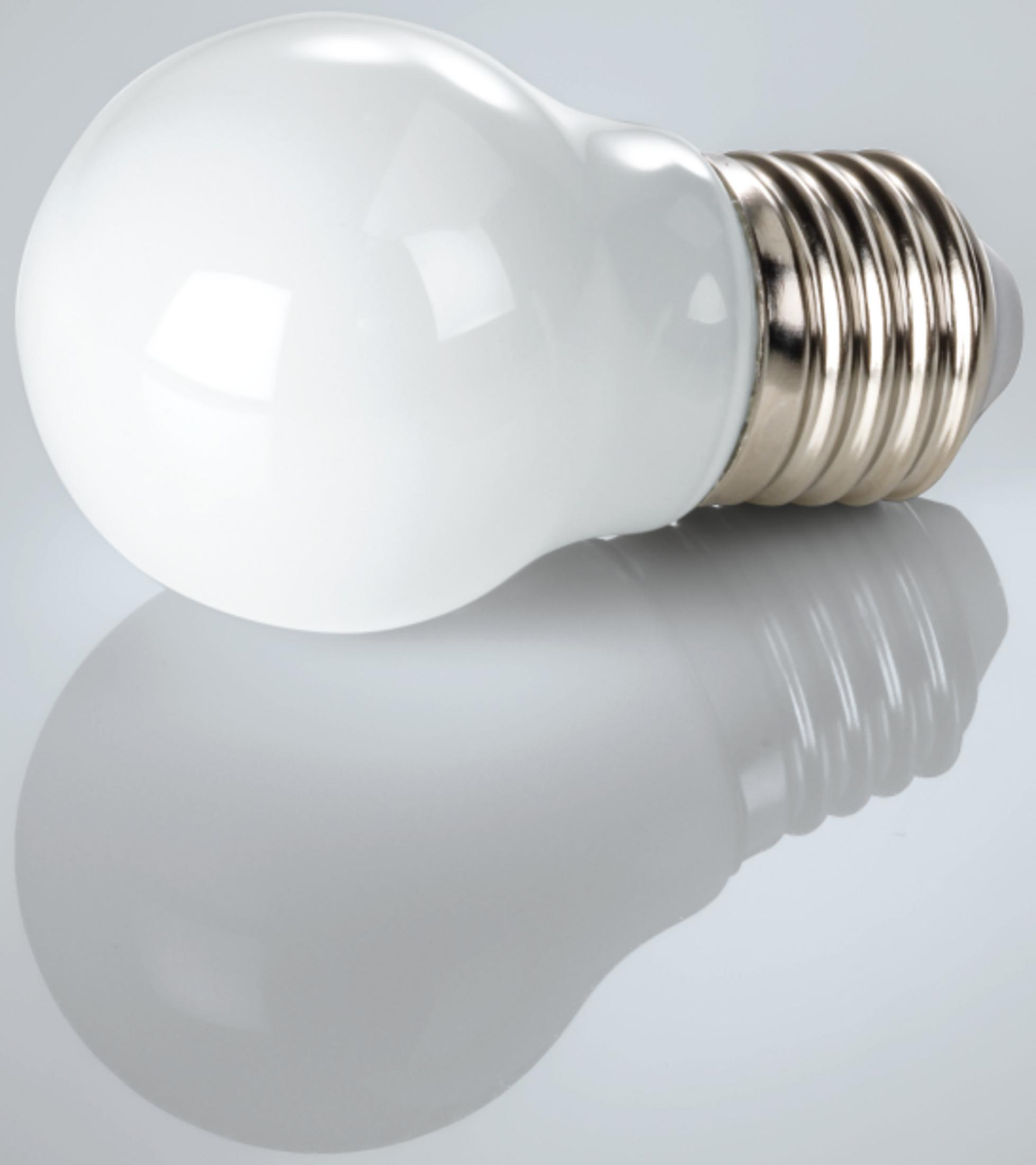 Biała żarówka leży na odblaskowej powierzchni.