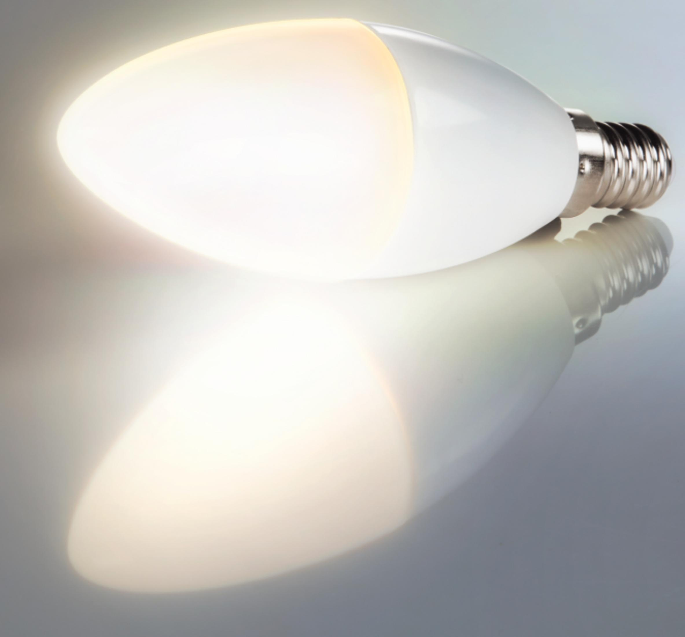 Eine leuchtende weiße Kerzen-LED-Lampe liegt auf einer spiegelnden Oberfläche.