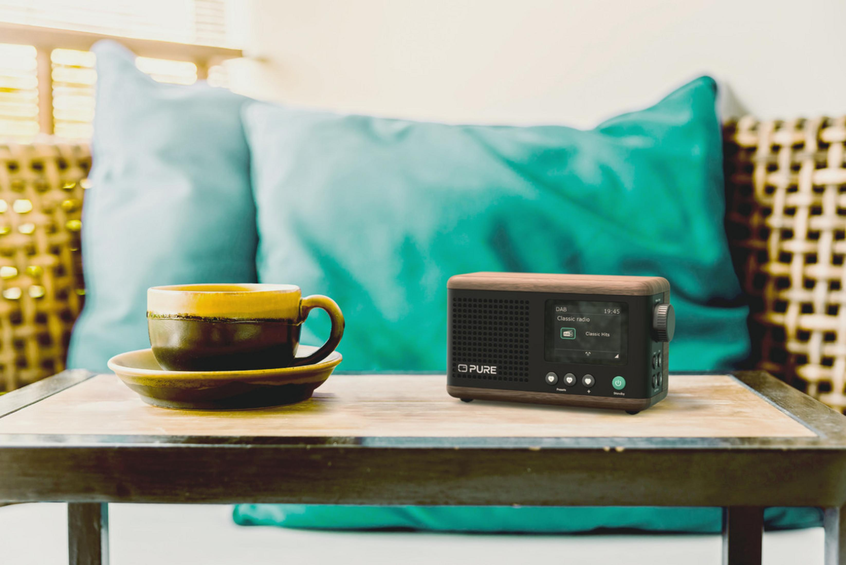 Radio in legno accanto a tazza da caffè marrone su tavolo con cuscini blu.