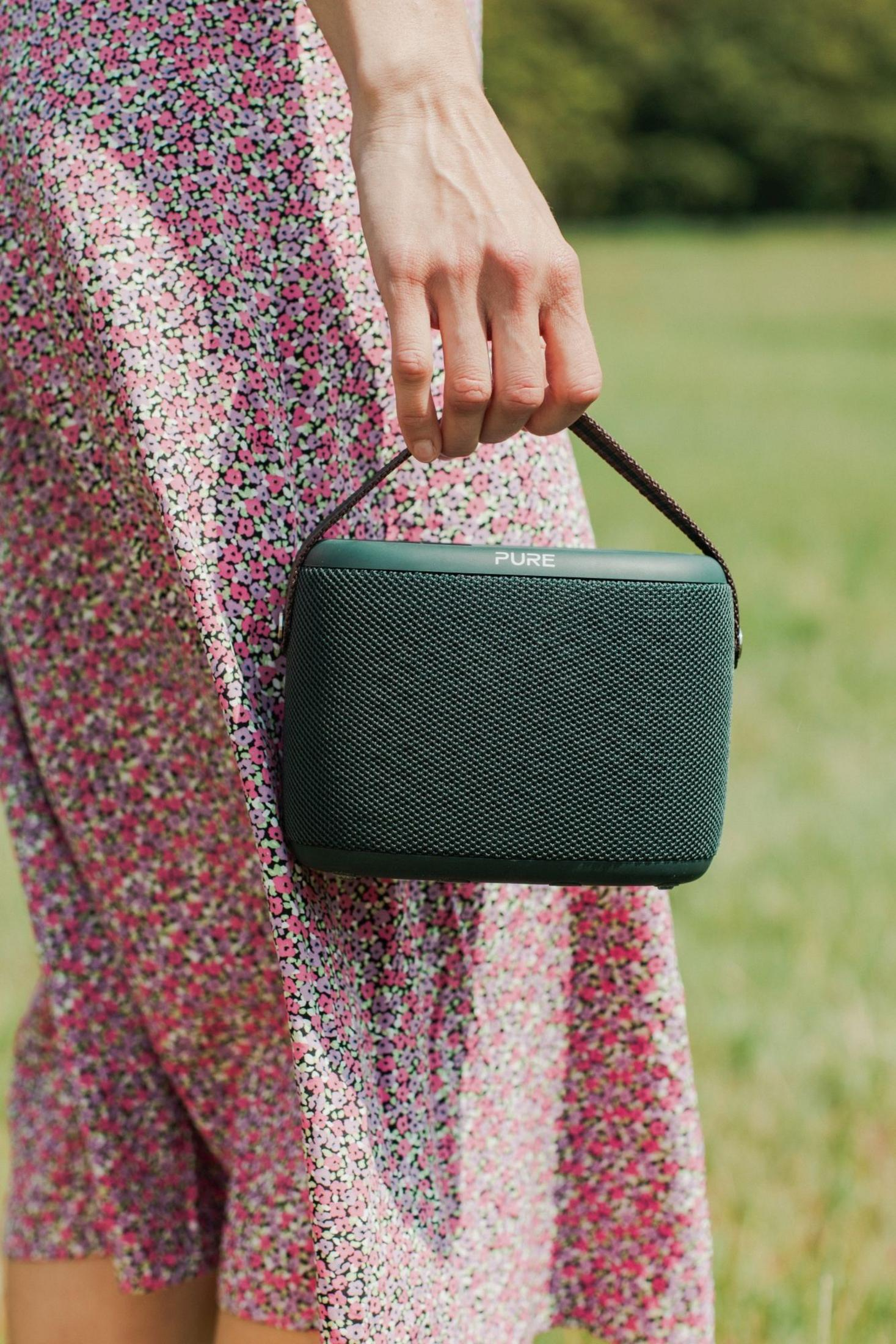 Person mit geblümtem Kleid hält eine grüne Lautsprecherbox mit Henkel.