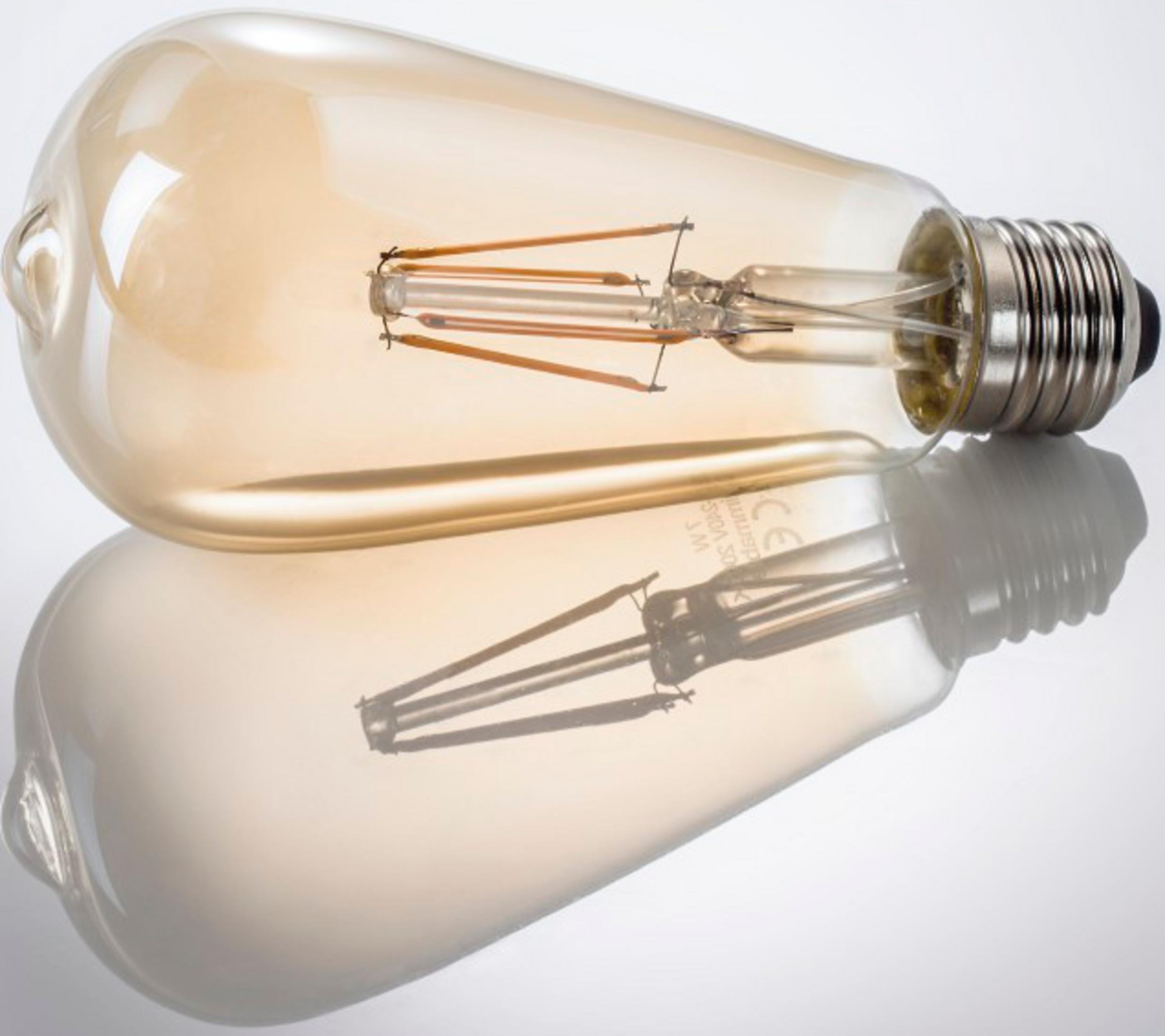 Una lampadina Edison ambrata con filamenti visibili giace su una superficie riflettente.